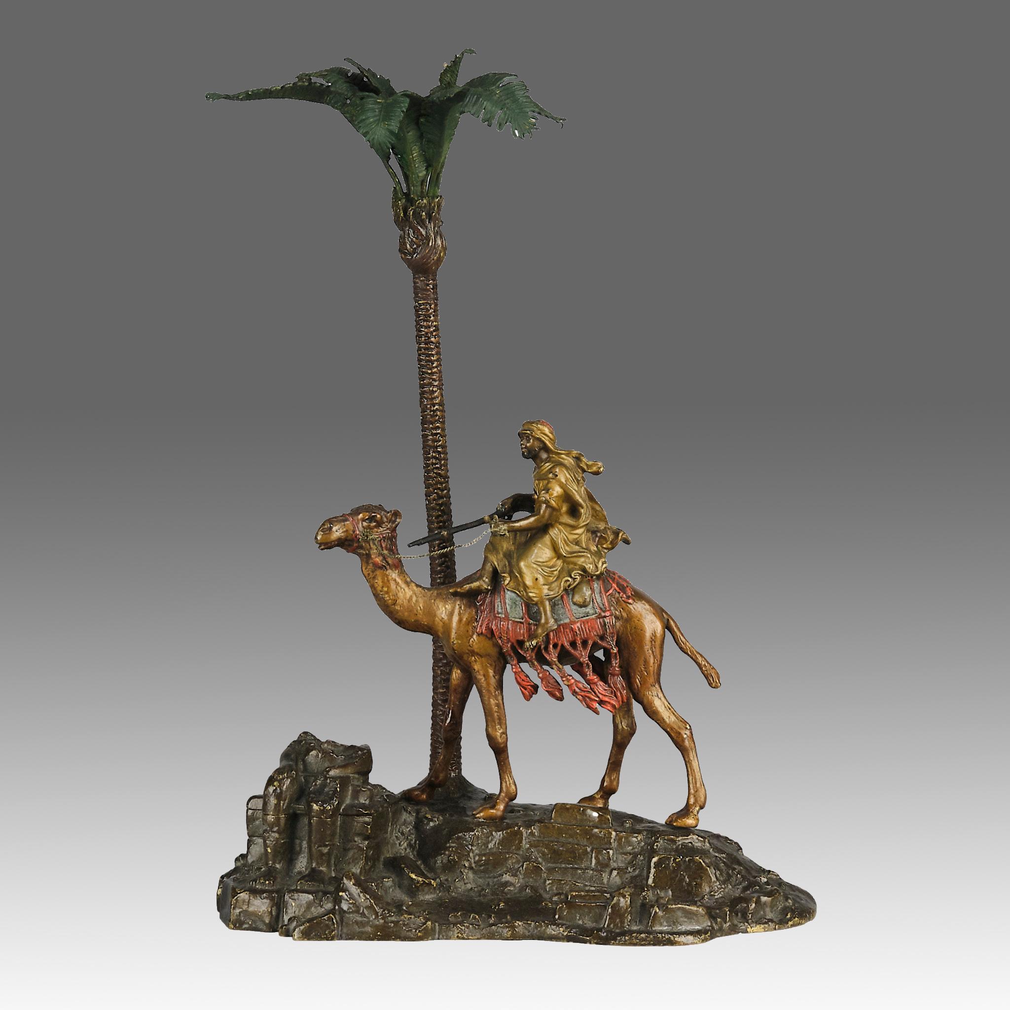 Magnífico tintero de bronce austriaco pintado en frío de principios del siglo XX, con un árabe armado montado en su camello junto a una palmera en un paisaje rocoso, con excelentes colores naturalistas y finos detalles acabados a mano, firmado con