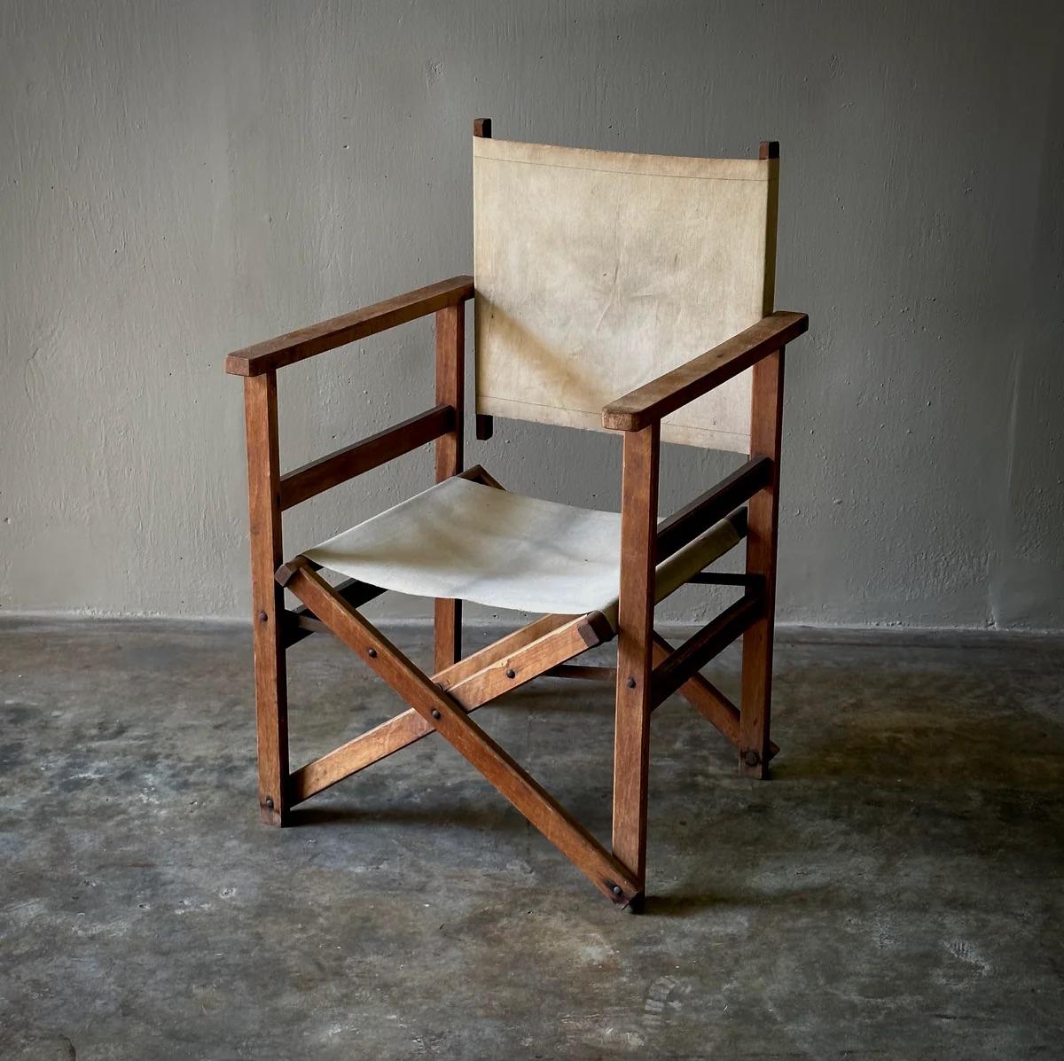 Esta silla de director de madera plegable de principios del siglo XX combina la practicidad con el encanto vintage, y presenta una tela original de color crema que luce con gracia su edad. Los pequeños detalles de tornillos metálicos del marco