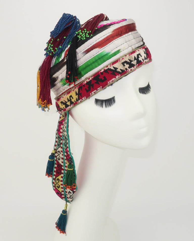 Early 20th century Central Asian quilted silk satin hat, probably Uzbekistan, decorated with a needlework brim and tail.  The body of the hat and tail are embellished with beaded silk tassels adding movement to the design.  The colorful pattern of