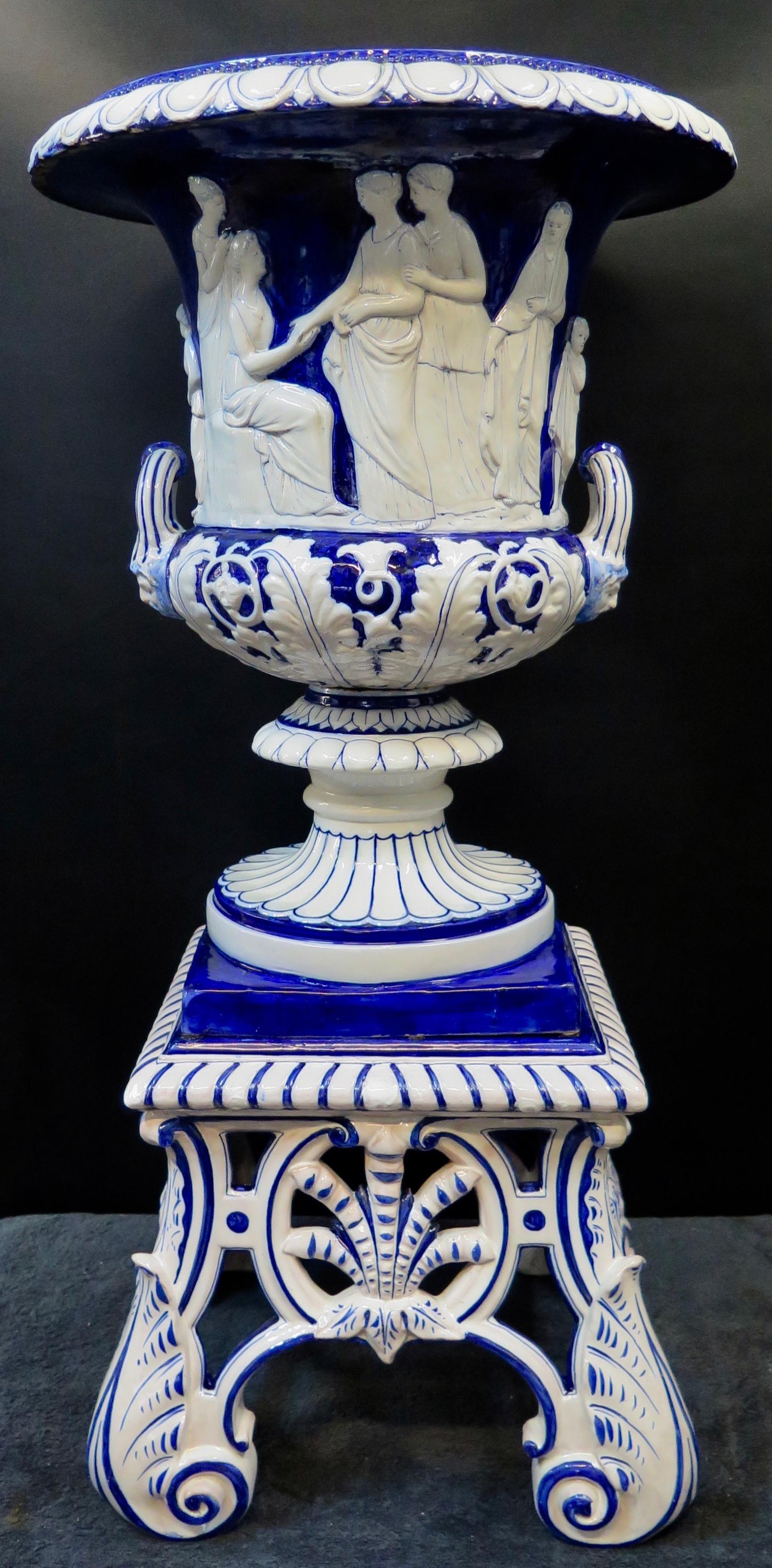 This early 20th century Continental terracotta planter is designed in a rich high glaze cobalt blue and white finish. The body of the planter features decorative applied handles that accent a frieze of women encircling the midpoint. This classical