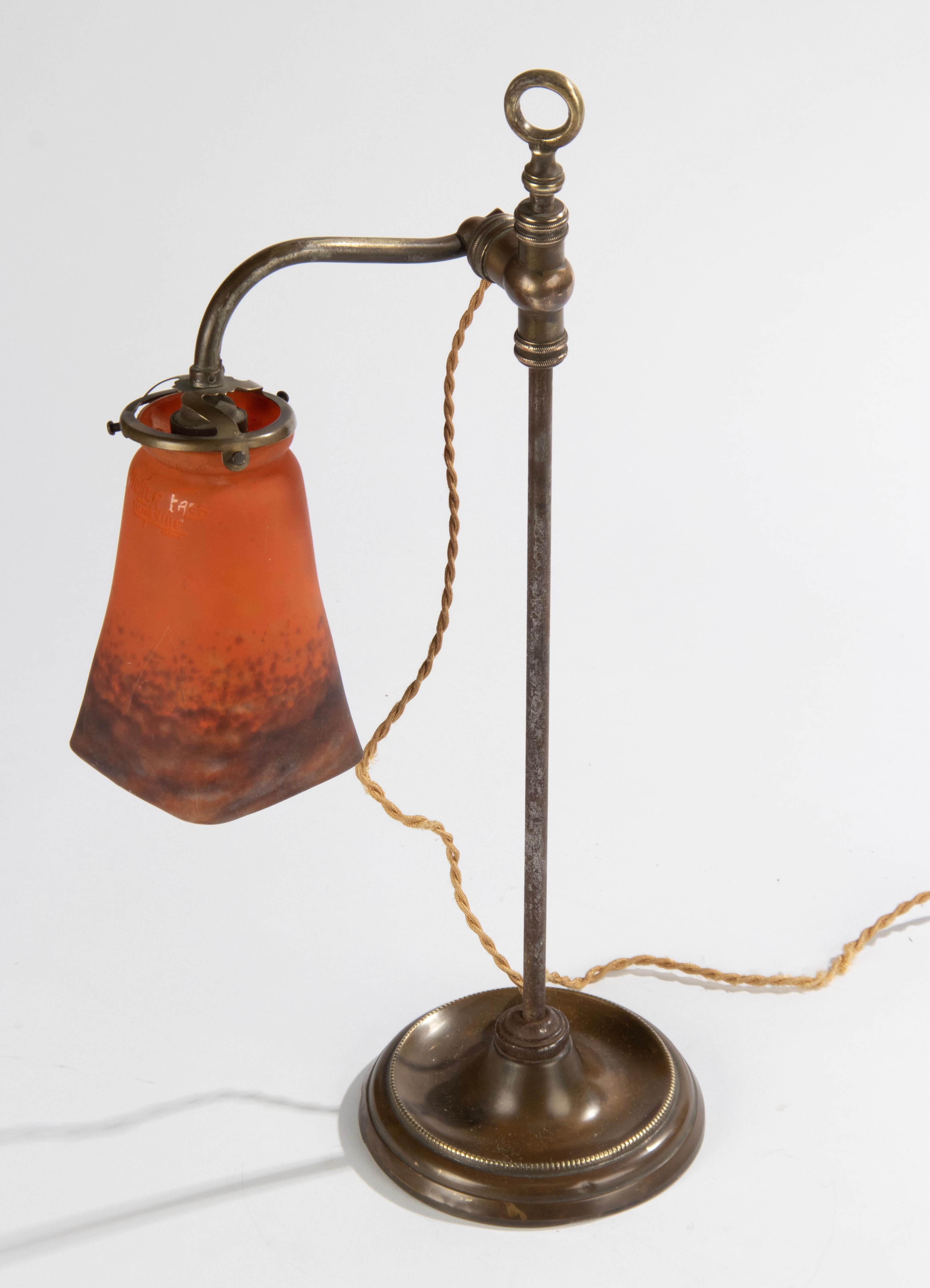An antique copper table lamp made of copper, the stem is made of metal. The tulip-shaped lampshade is made of paste-glass (Patte Verte) and signed by Muller Fréres, Lunneville, France. In side a bajonet socket. 
When the light is switched on it