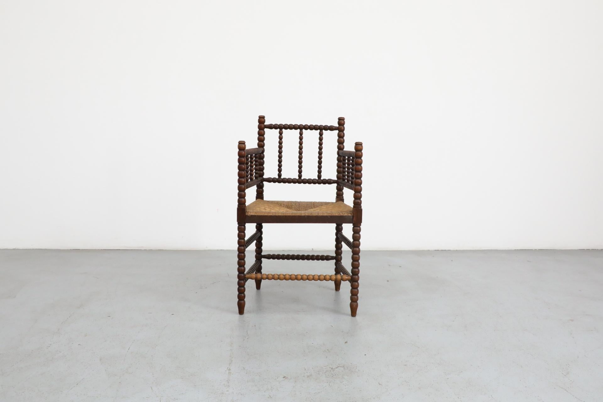 Fauteuil bobine classique de style cottage en bois magnifiquement vieilli et teinté avec assise en rotin et cadre décoratif sculpté à la main. En état d'origine avec une usure conforme à l'âge et à l'utilisation.