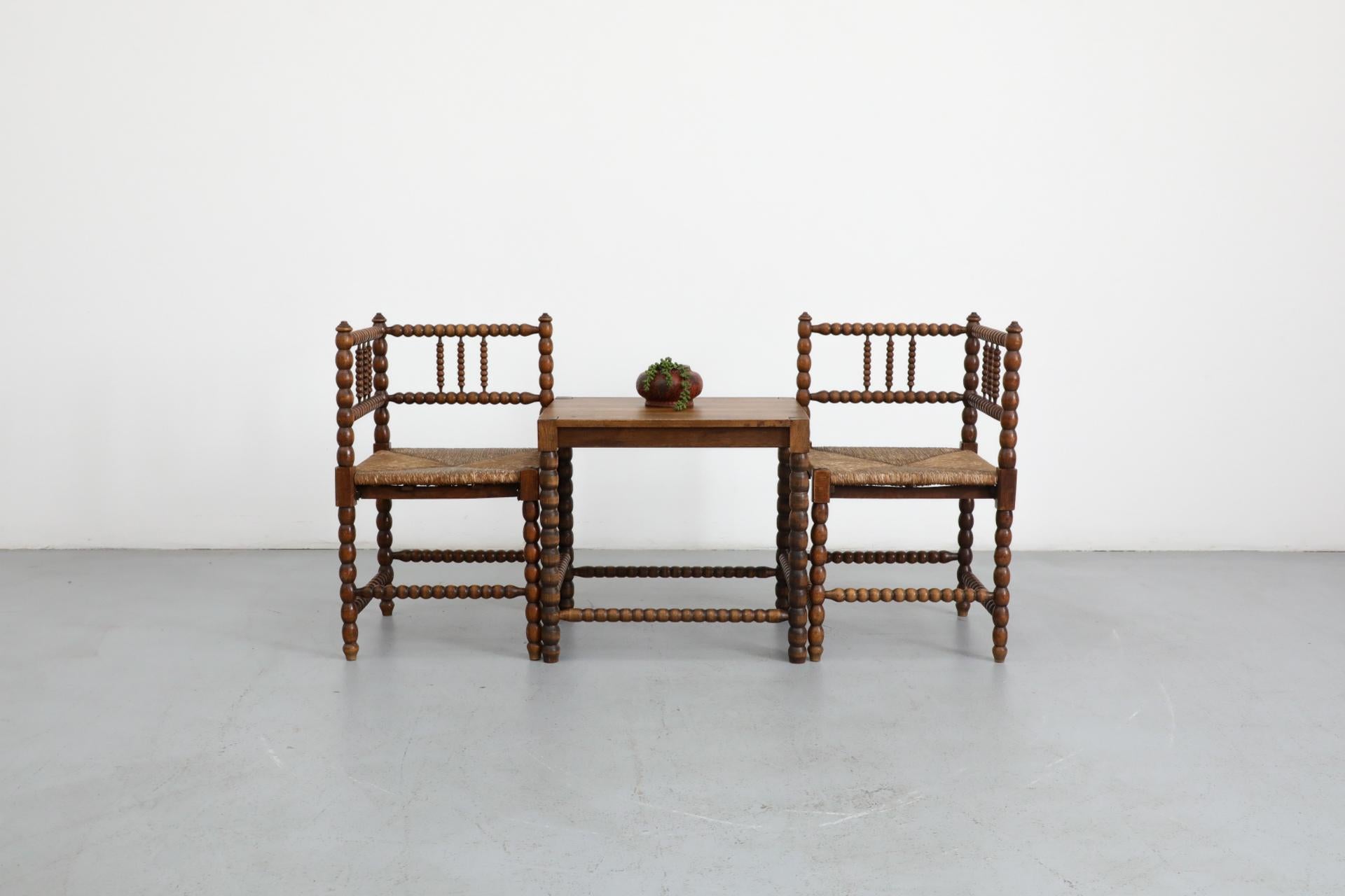 Sillas rinconeras clásicas de estilo rústico y mesa de salón a juego, de madera bellamente envejecida y entonada, con asiento de junco y marco decorativo tallado a mano. Todo en estado original, con el desgaste propio de la edad y el uso. Se venden