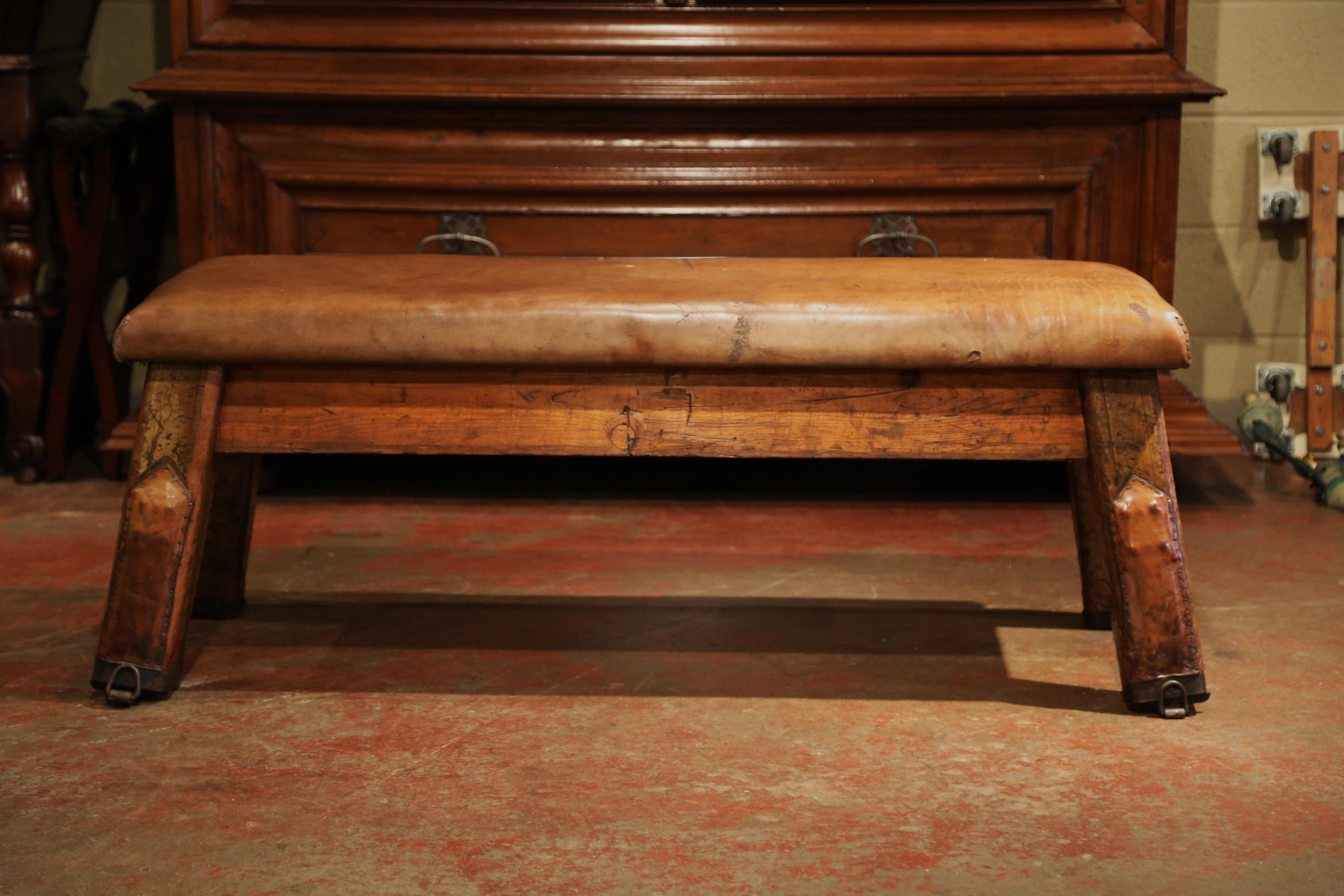 This antique leather bench was crafted in the Czech Republic, circa 1920. The rustic exercising seat features four angled wooden legs recovered with brown leather. The rounded, original top is also covered with a nicely aged leather upholstery. This