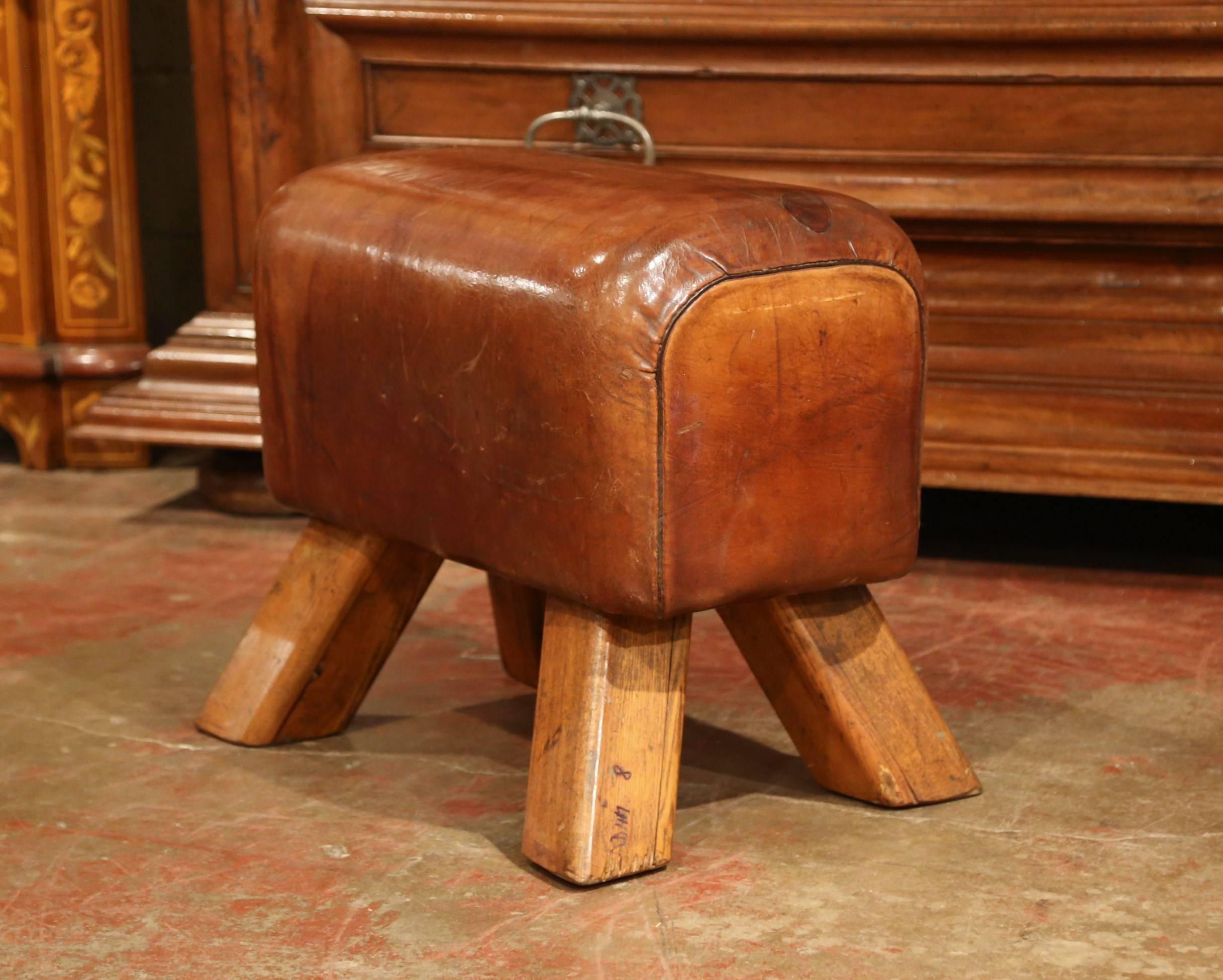 This antique, gymnasium leather pommel horse bench was crafted in the Czech Republic, circa 1920. The rustic stool features four angled wooden legs and the seat is upholstered with the original brown leather. This sturdy piece is in excellent