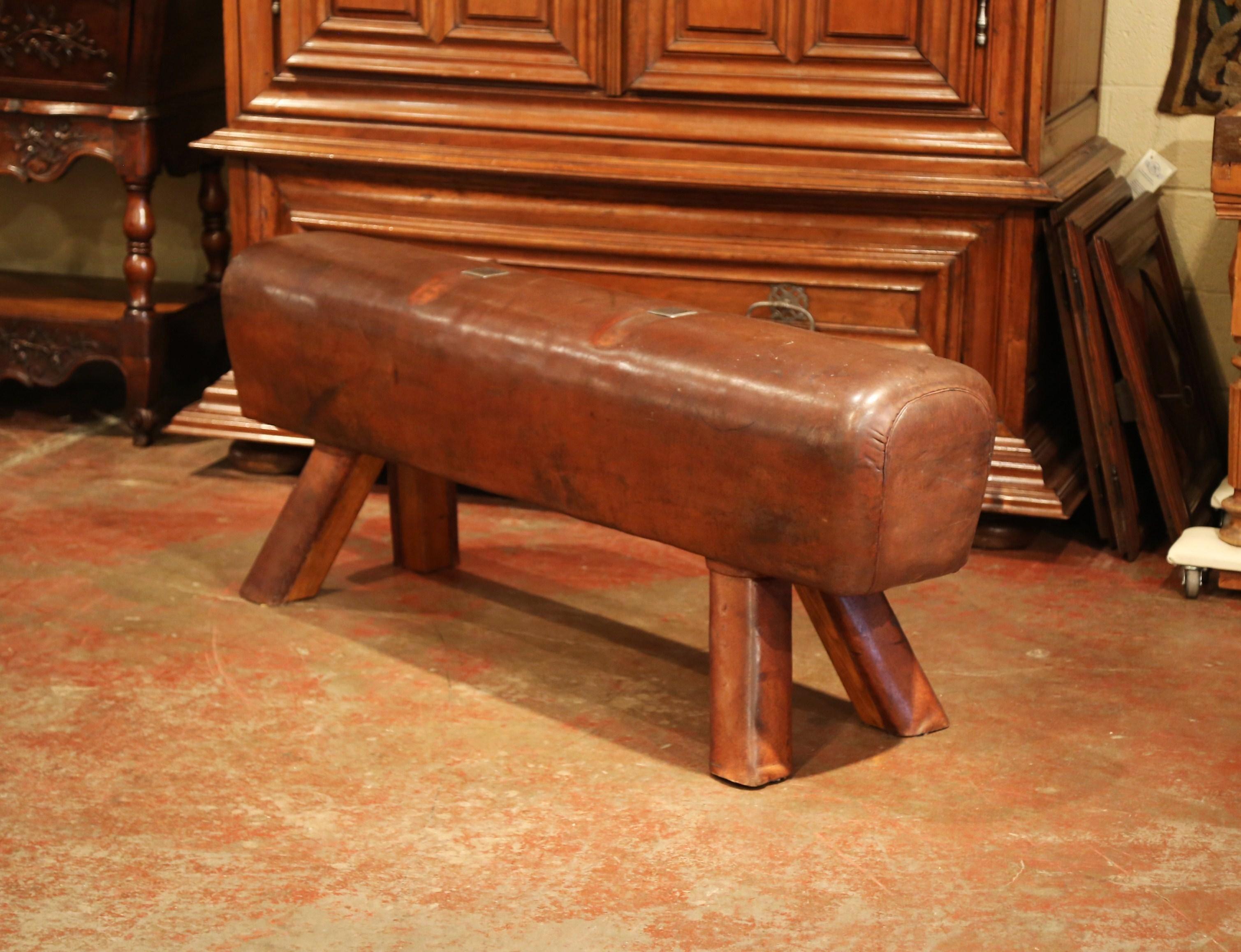 This antique, long gymnasium leather pommel horse bench was crafted in the Czech Republic, circa 1920. The rustic piece sits on four wooden legs covered with original leather; the long seat is upholstered with the original patinated brown leather