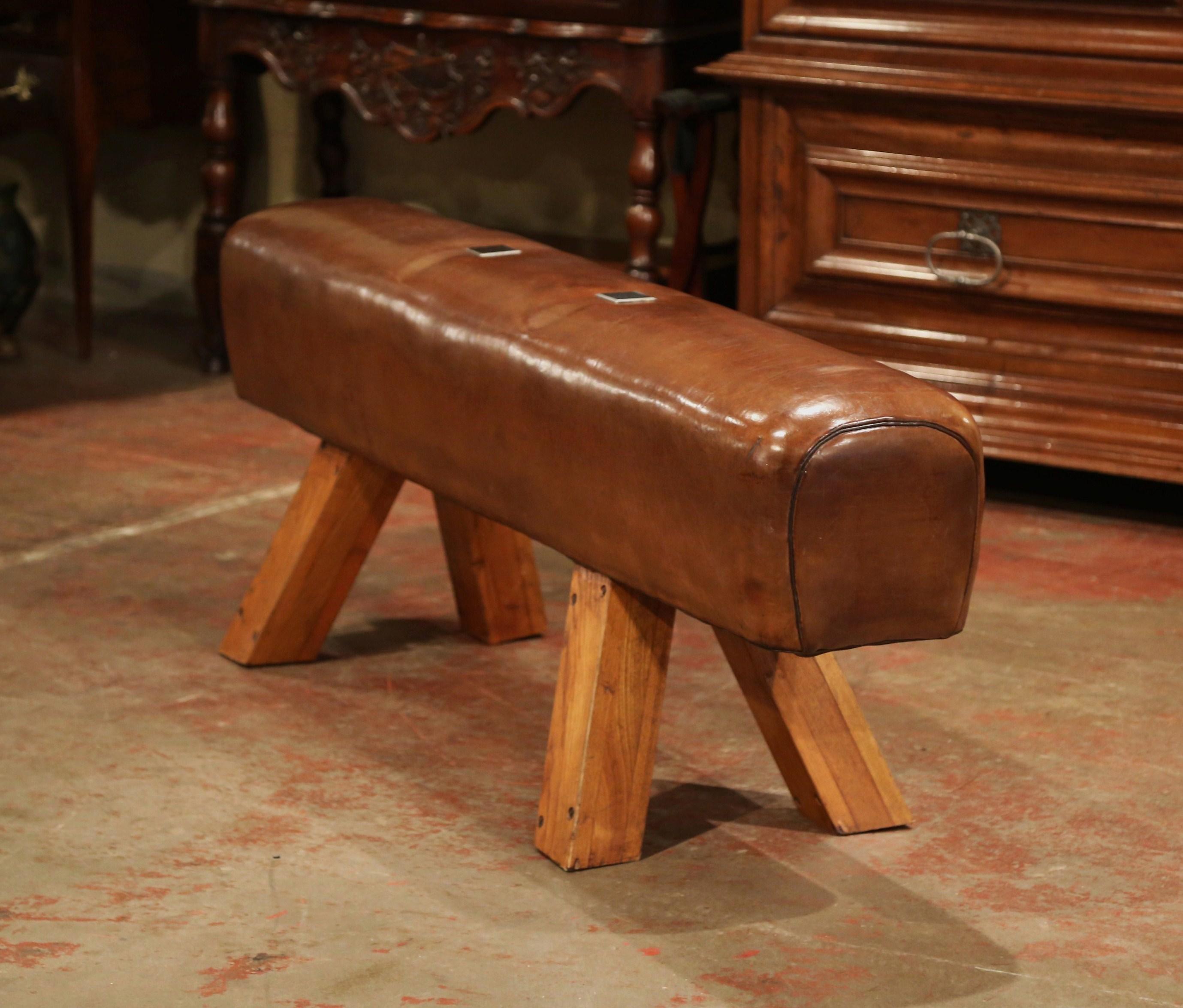 This antique, long gymnasium leather pommel horse bench was crafted in the Czech Republic, circa 1920. The rustic piece sits on four slant wooden legs and the long seat with rounded corners is upholstered with the original patinated brown leather;