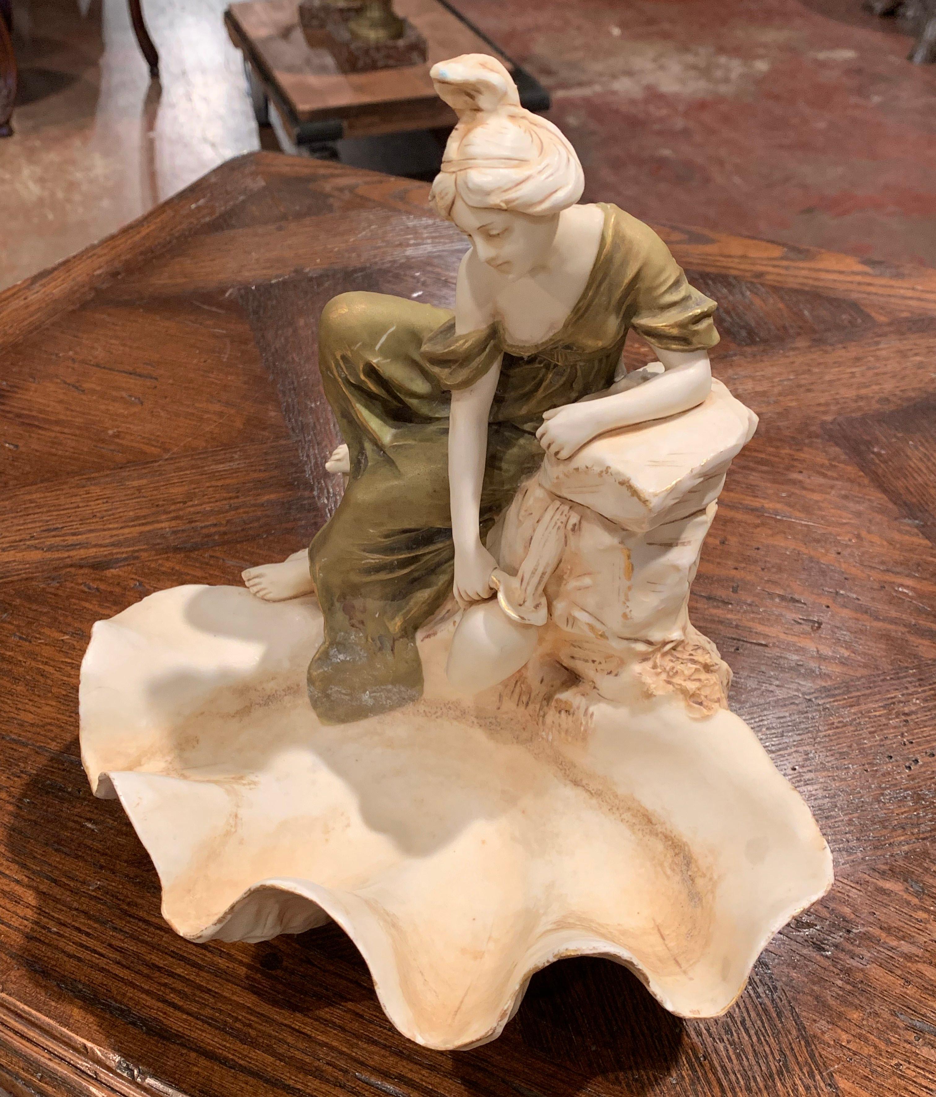 Fabriquée en République tchèque vers 1930, cette sculpture Art déco représente une femme assise sur le bord d'un bassin et remplissant sa cruche d'eau. La composition du plat sculpté est en excellent état, avec une riche finition patinée, et