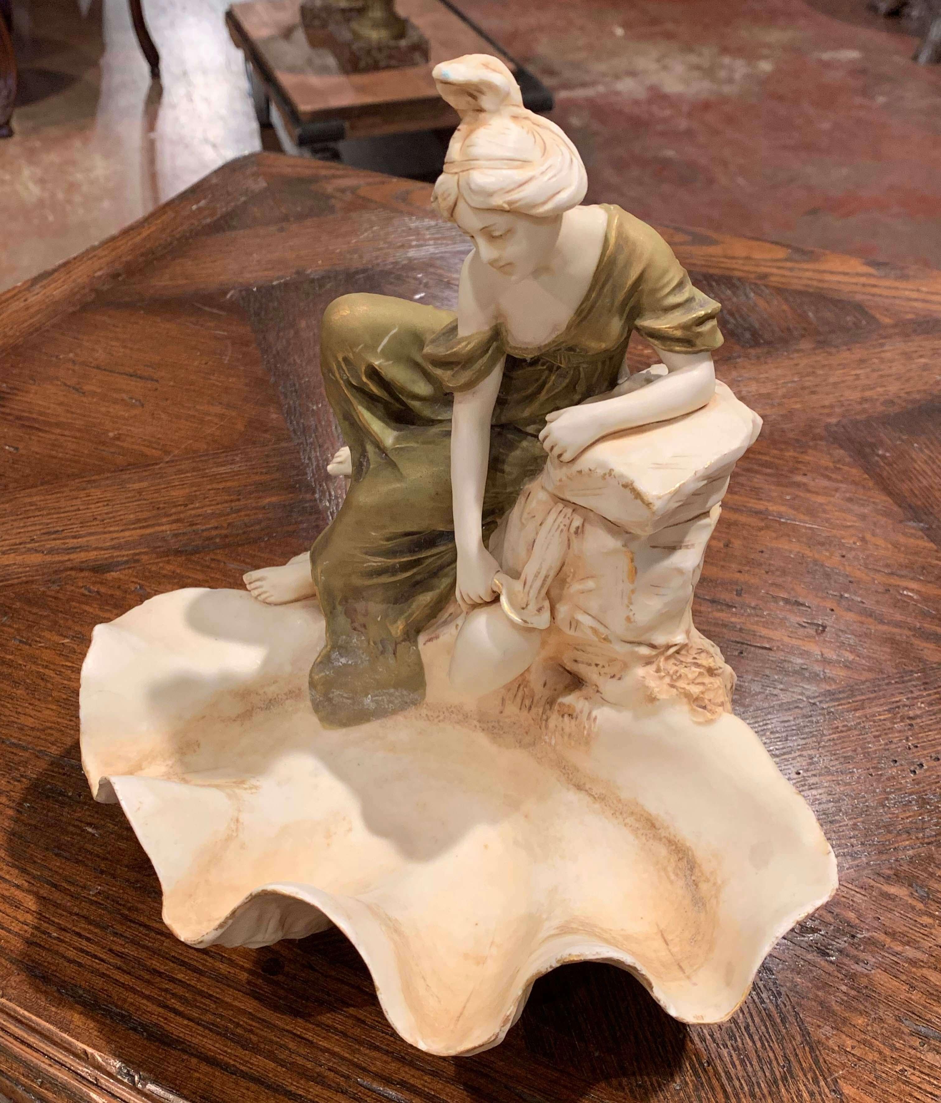Decora el tocador o el tocador de una mujer con este elegante plato escultórico bohemio de cerámica vintage, fabricado en la República Checa hacia 1930. La escultura Art Decó presenta una estatua femenina con un vestido verde dorado, apoyada en el