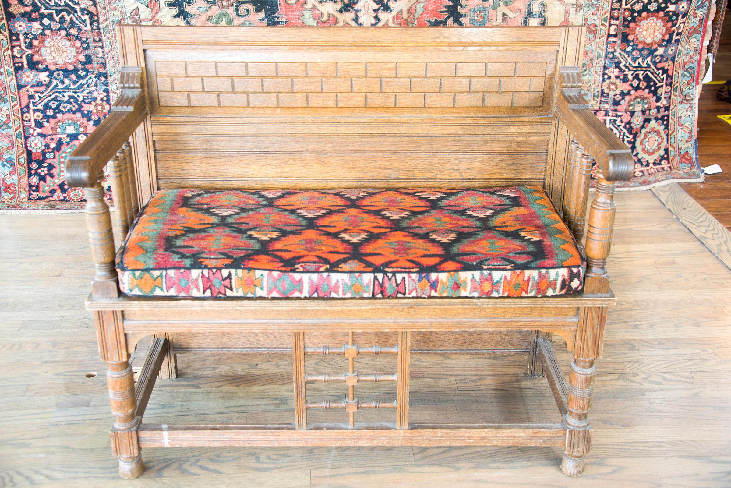 An early 20th century Danish oak bench with paneled back, turned arm supports and legs, with a newly upholstered seat cushion using a vintage Qazvin kilim rug with myriad stylized flowers woven in brilliant golds, turquoises, pinks, oranges, and