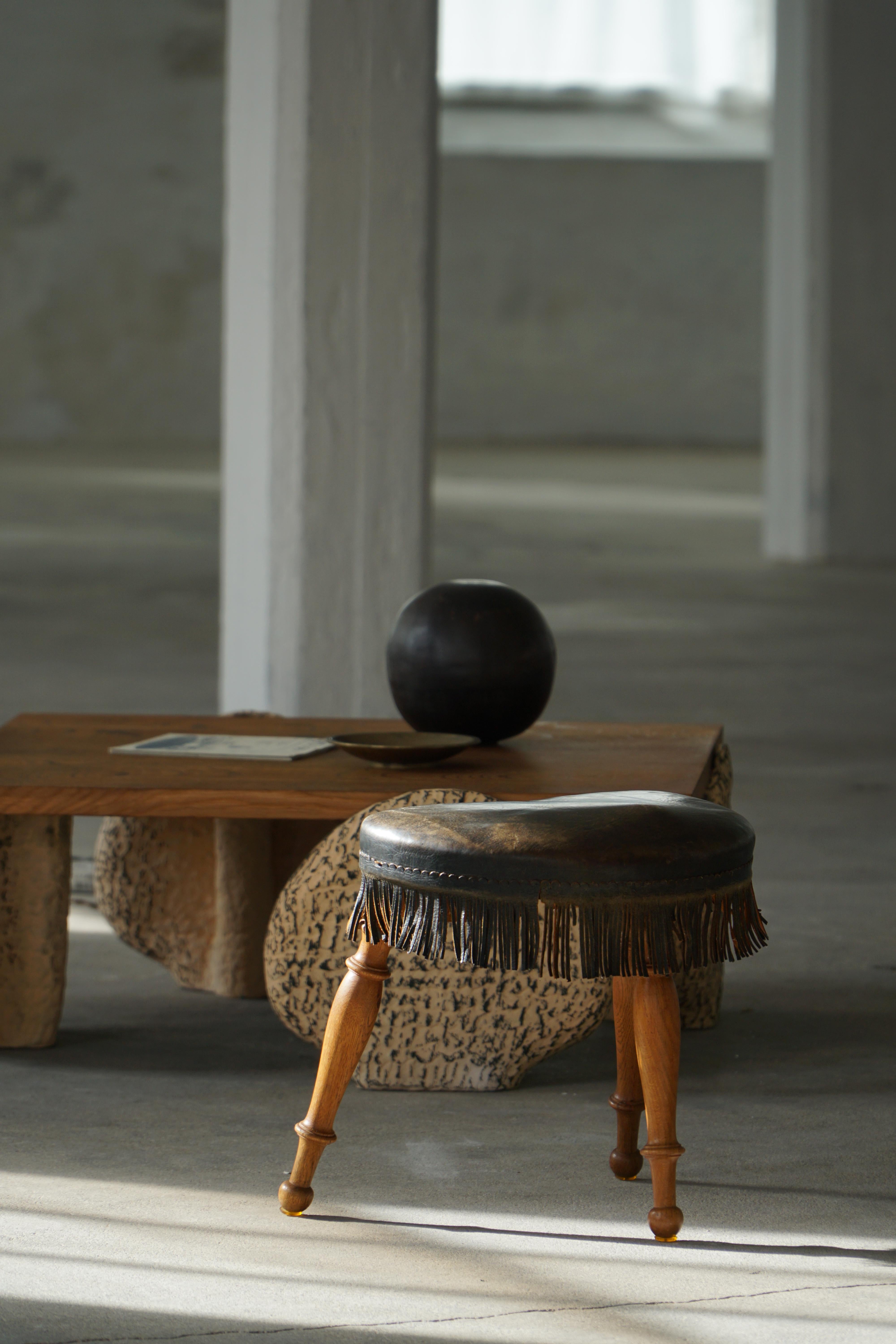 A rare and charming Danish stool from the 1930s, handcrafted in oak with a leather-upholstered seat. This three-legged design features a subtly contoured seat with a defined “front” and “back,” shaped to accommodate the sitter comfortably,