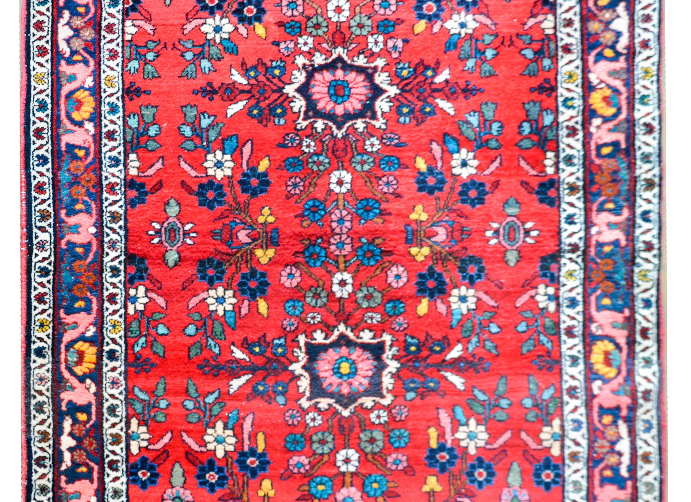 A wonderful early 20th century Persian Dargazin rug with two small stylized floral medallions amidst a field of more flowers and set against a crimson background. The border is simple with three petite floral patterned stripes.