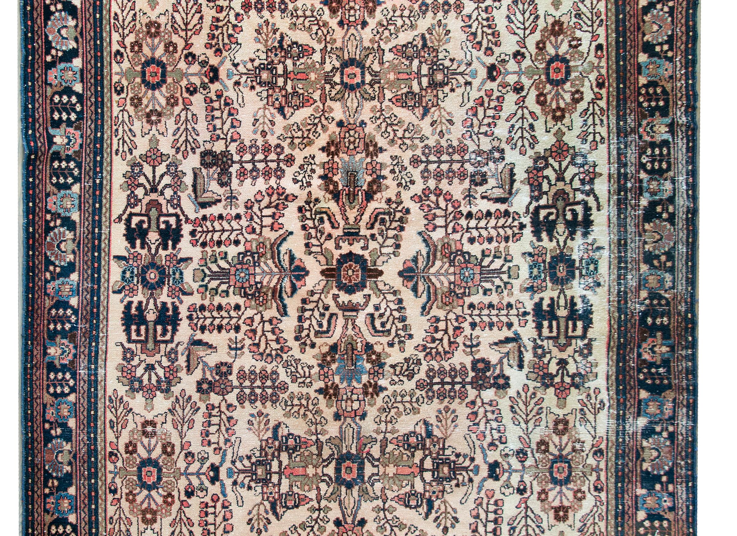 A stunning early 20th century Persian Dargazin rug with a beautiful mirrored floral and tree-of-life pattern woven in unique indigos, greens, golds, and pinks, all set against a cream colored background, and surrounded by a complex border with a