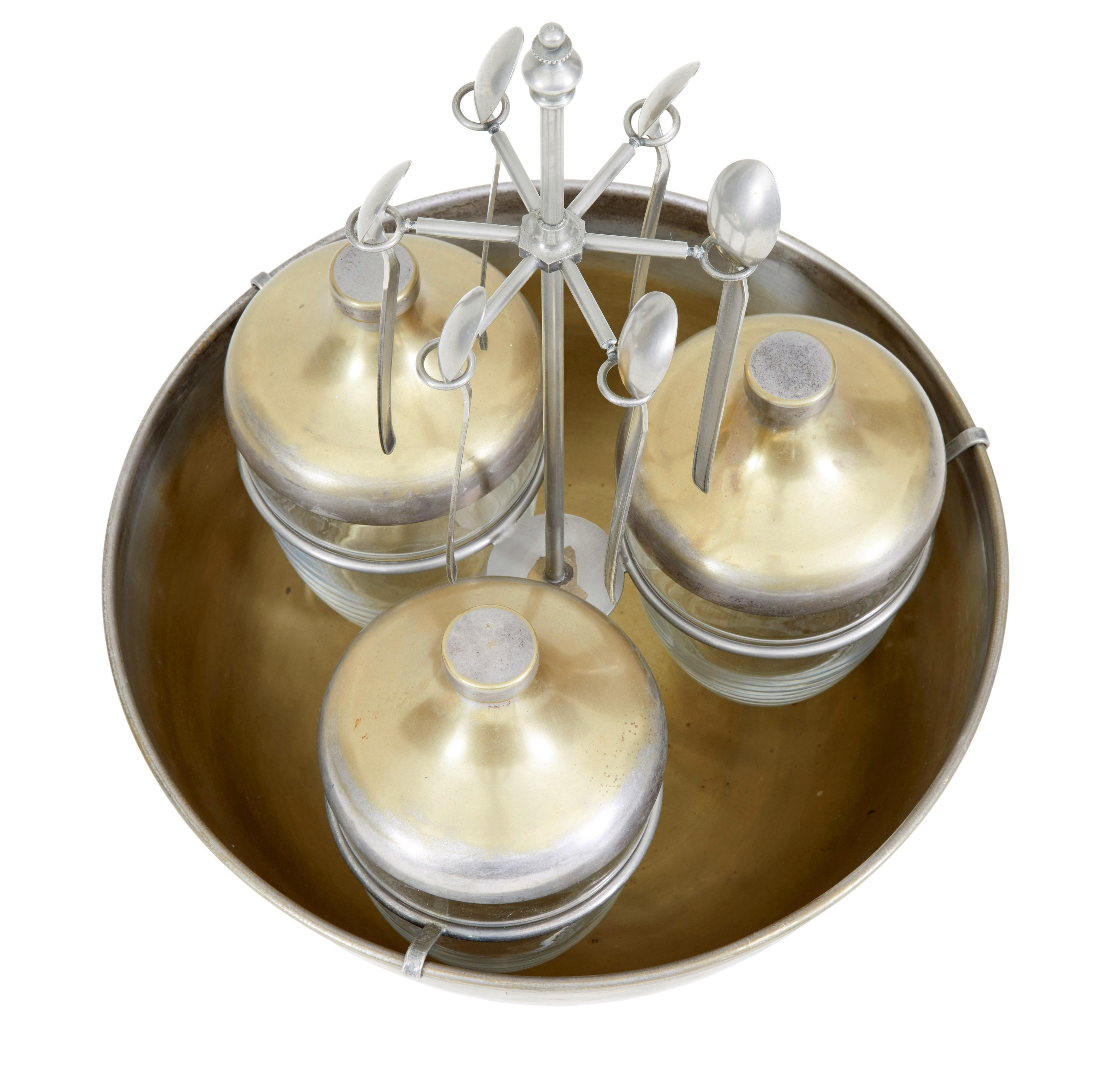 Interesting caviar set, circa 1920.

Comprising of four elements. Bowl, three jars with lids, holding rack and spoons.

Made from steel and gilded which has mostly worn away. The steel holder keeps the glass jars elevated and holds 6 spoons,