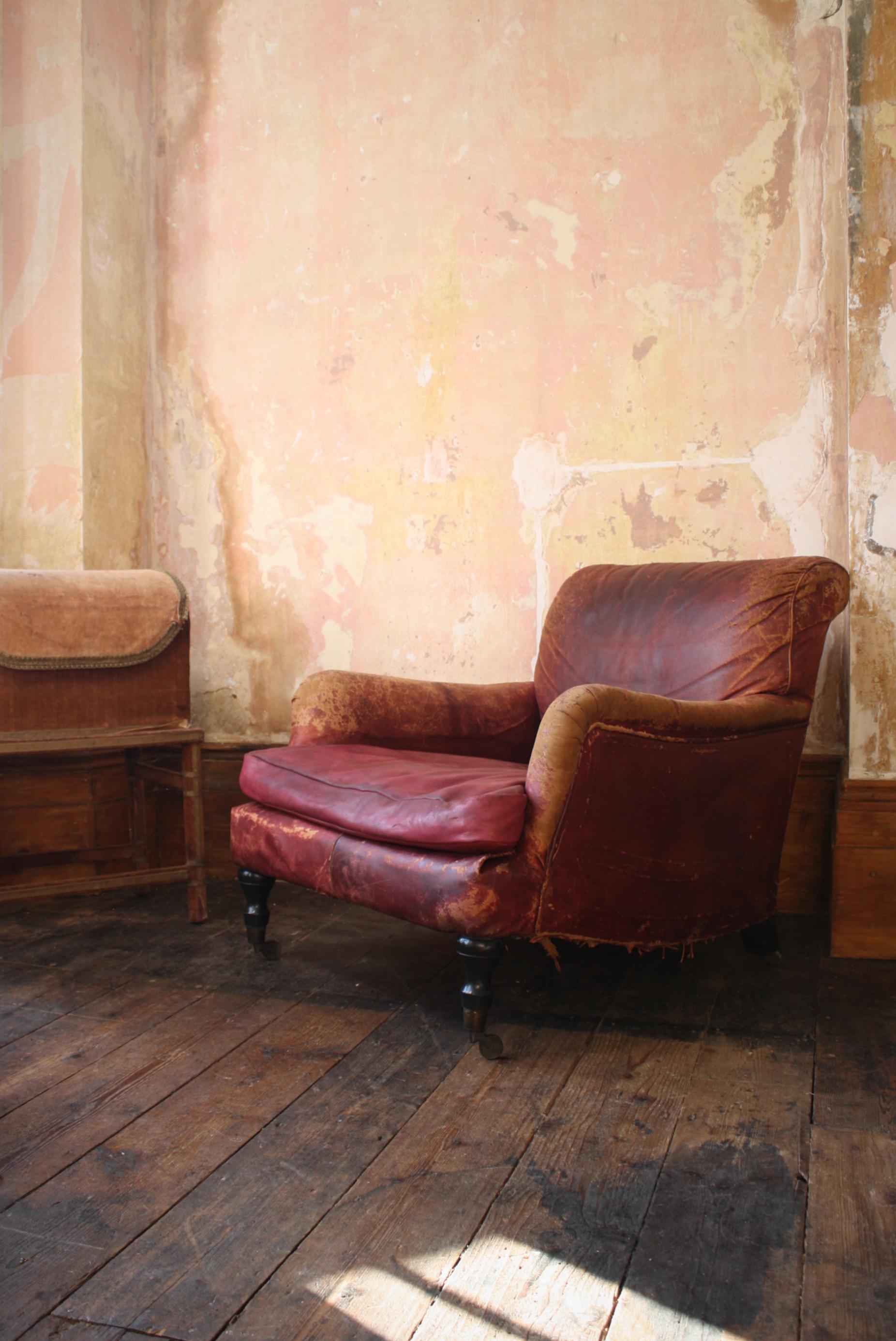 A beautifully worn red leather deep seated easy armchair, on turned ebonised front legs, brass cup castors.

The original removable feather filled cushion with a later leather cover, all round wear marks and abrasions to the leather, some elderly