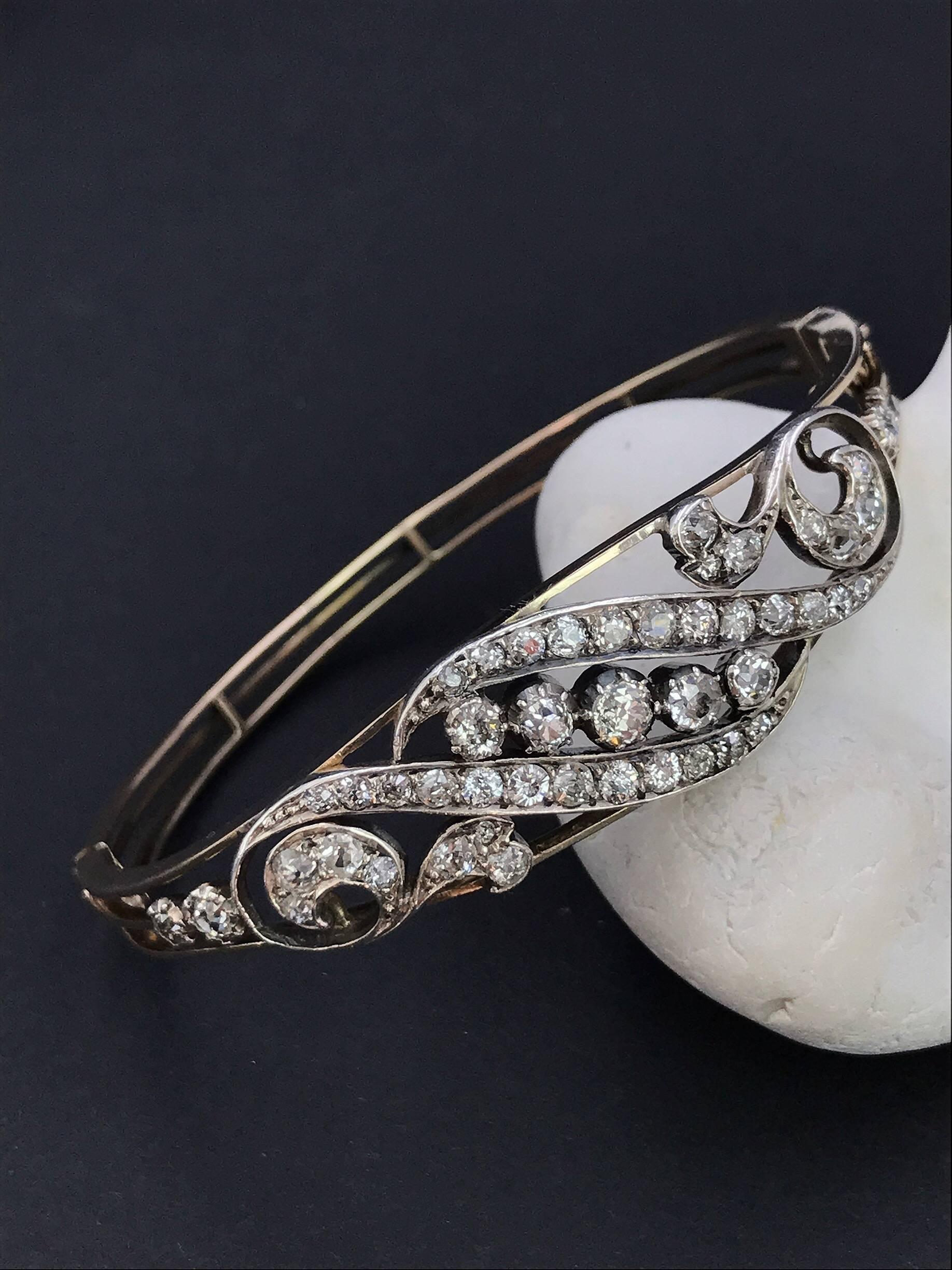 An early 20th century gold, diamond hinged bangle. Set in 9ct gold and silver. The old-cut diamond scrolling foliate motif, to the openwork half-bangle. Estimated total diamond weight 2.30cts. Inner diameter 5.7cms. Weight 14.6gms. Diamonds fairly