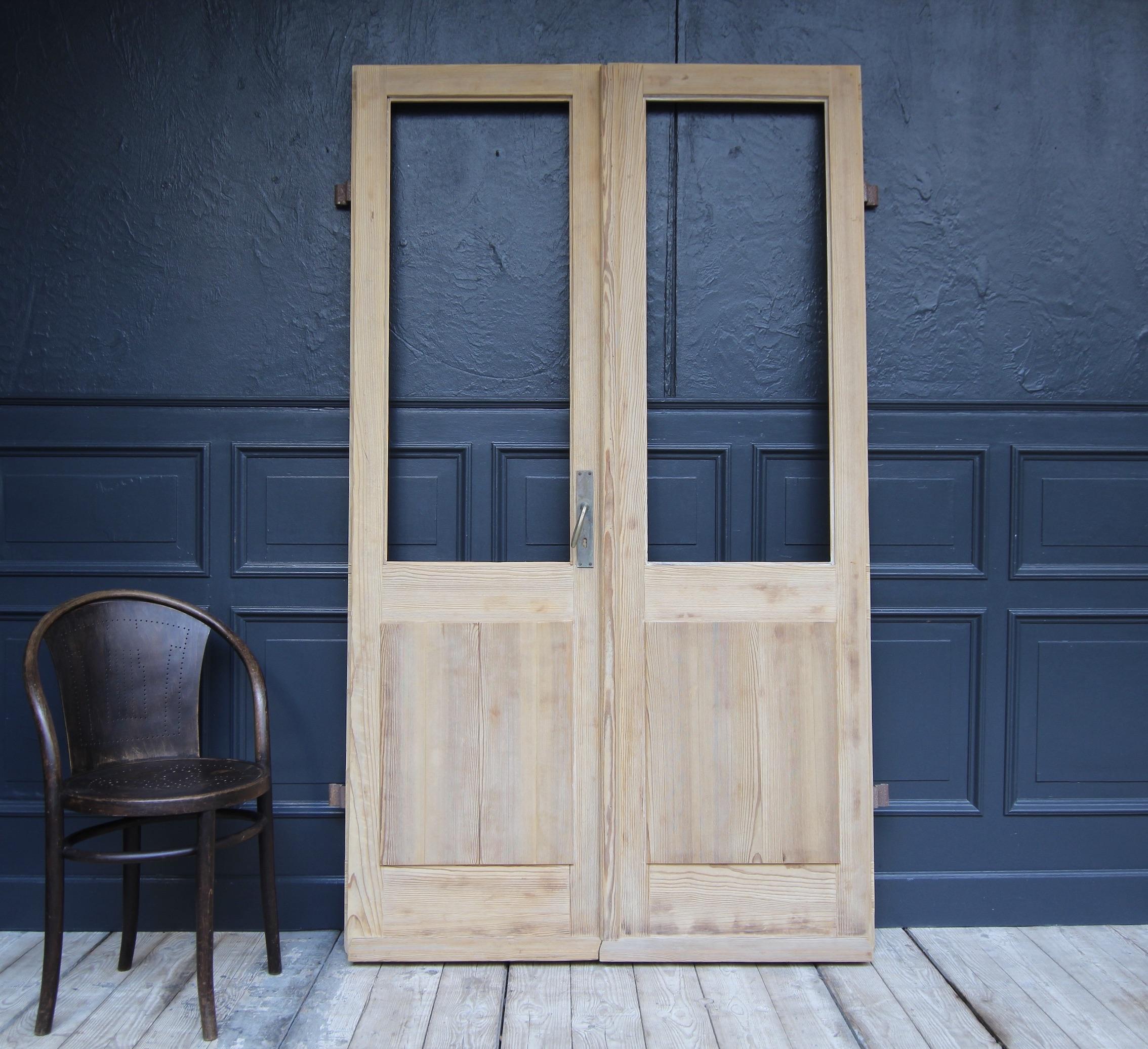 Pine wood double door from Switzerland. Early 20th century. Unrestored.

Consisting of two originally half-glazed doors in frame and panel construction with large cranked iron fittings on the outside. 
Without glass panes.

Dimensions: 
209 cm high