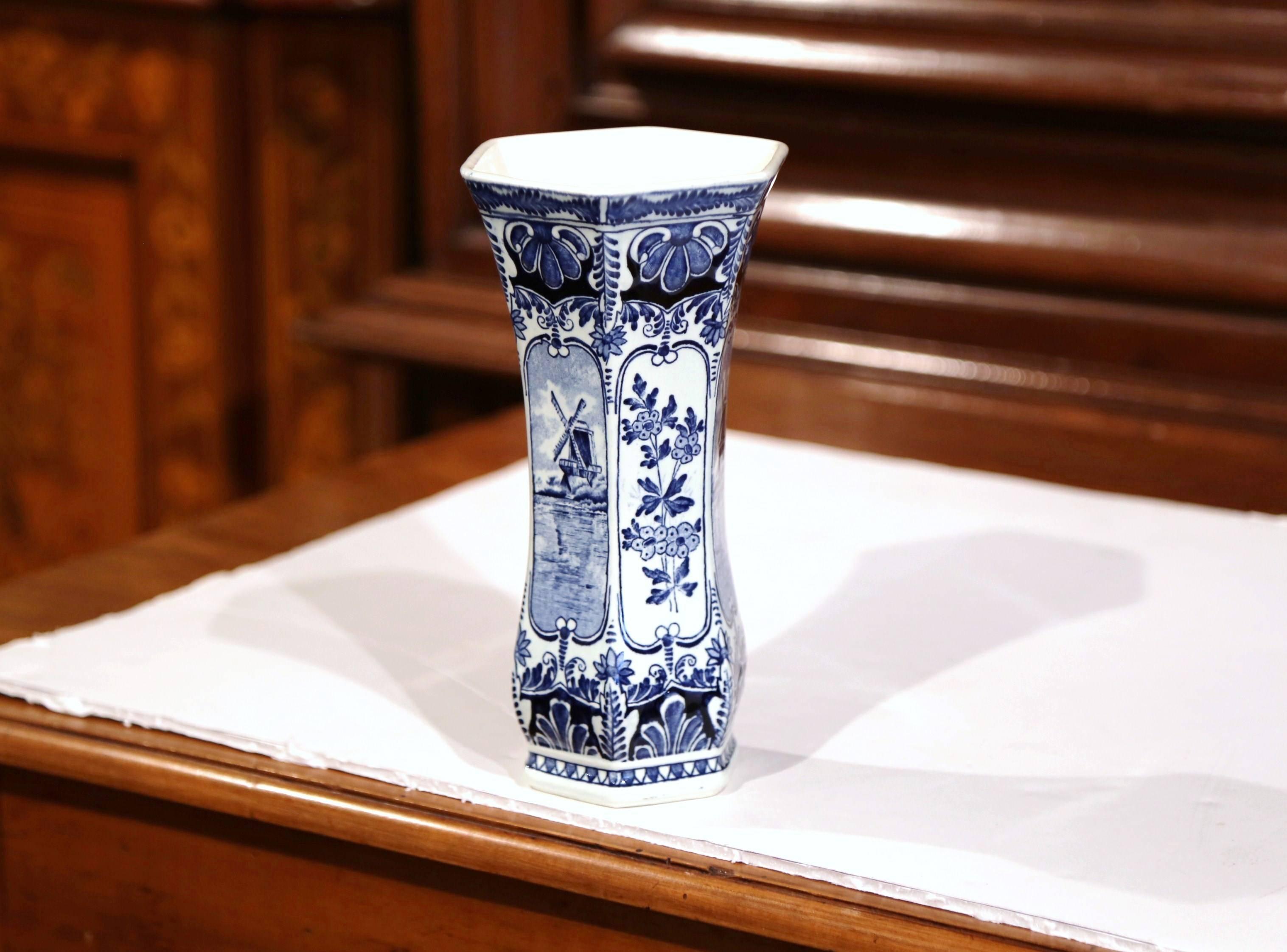 This vintage Delft vase was created in Maastricht, Netherlands, circa 1930. The ceramic, hexagonal flower vase features traditional hand-painted scenes including the a windmill, lake and flower decorations. It is stamped on the bottom, Royal Sphinx,