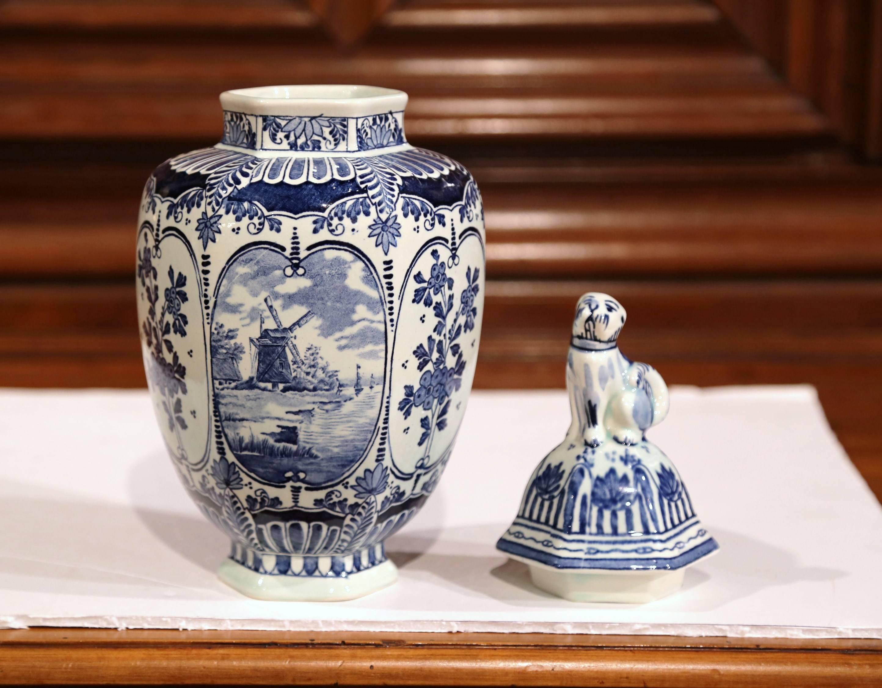 Ce magnifique pot de gingembre vintage a été fabriqué en Hollande, vers 1920. Le potiche en céramique présente des scènes peintes à la main avec des moulins à vent et des fleurs de la Hollande classique. La jarre traditionnelle bleue et blanche a un