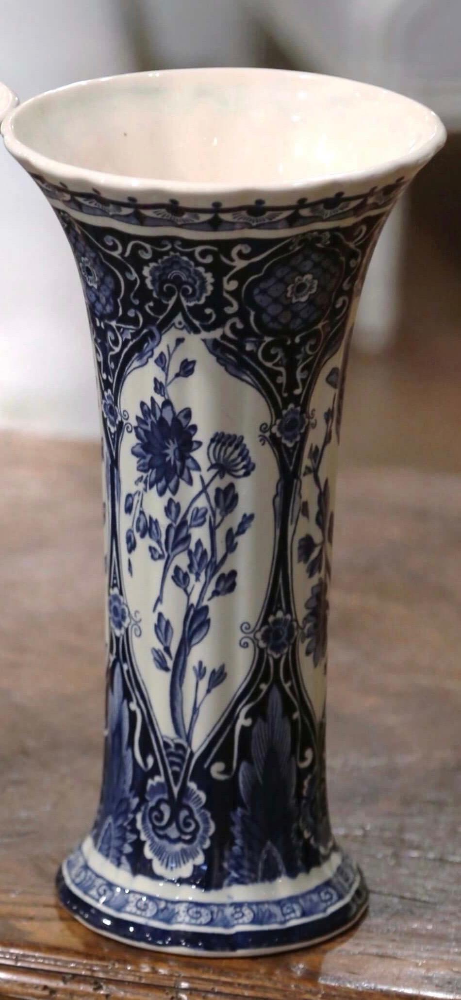 Decorate a shelf or console table with this elegant antique Delft style vase. Crafted in Netherlands circa 1920, the hand-painted trumpet vase is round in shape over a long, elegant, fluted neck. Each vintage vessel is painted in the blue and white