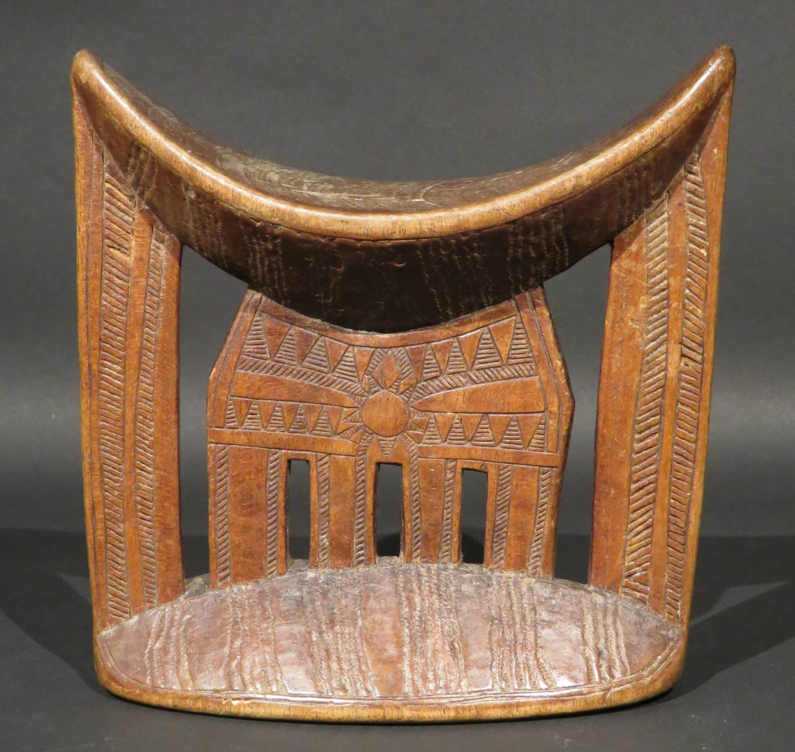 Showing a crescent shaped rest braced by flattened supports atop a cupped base, decorated with carved incised geometric motifs and exhibiting a mellow patina overall.