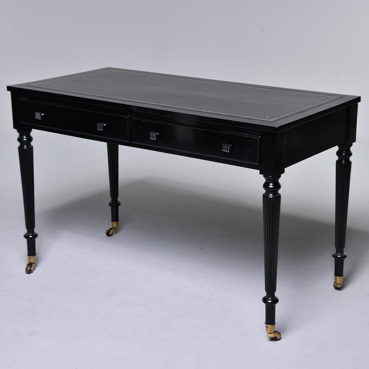 English mahogany desk has a new, professionally applied ebonized finish, new leather top with tooled and silvered border, two functional drawers with new polished nickel hardware, turned and reeded legs with original brass casters, circa 1920s.