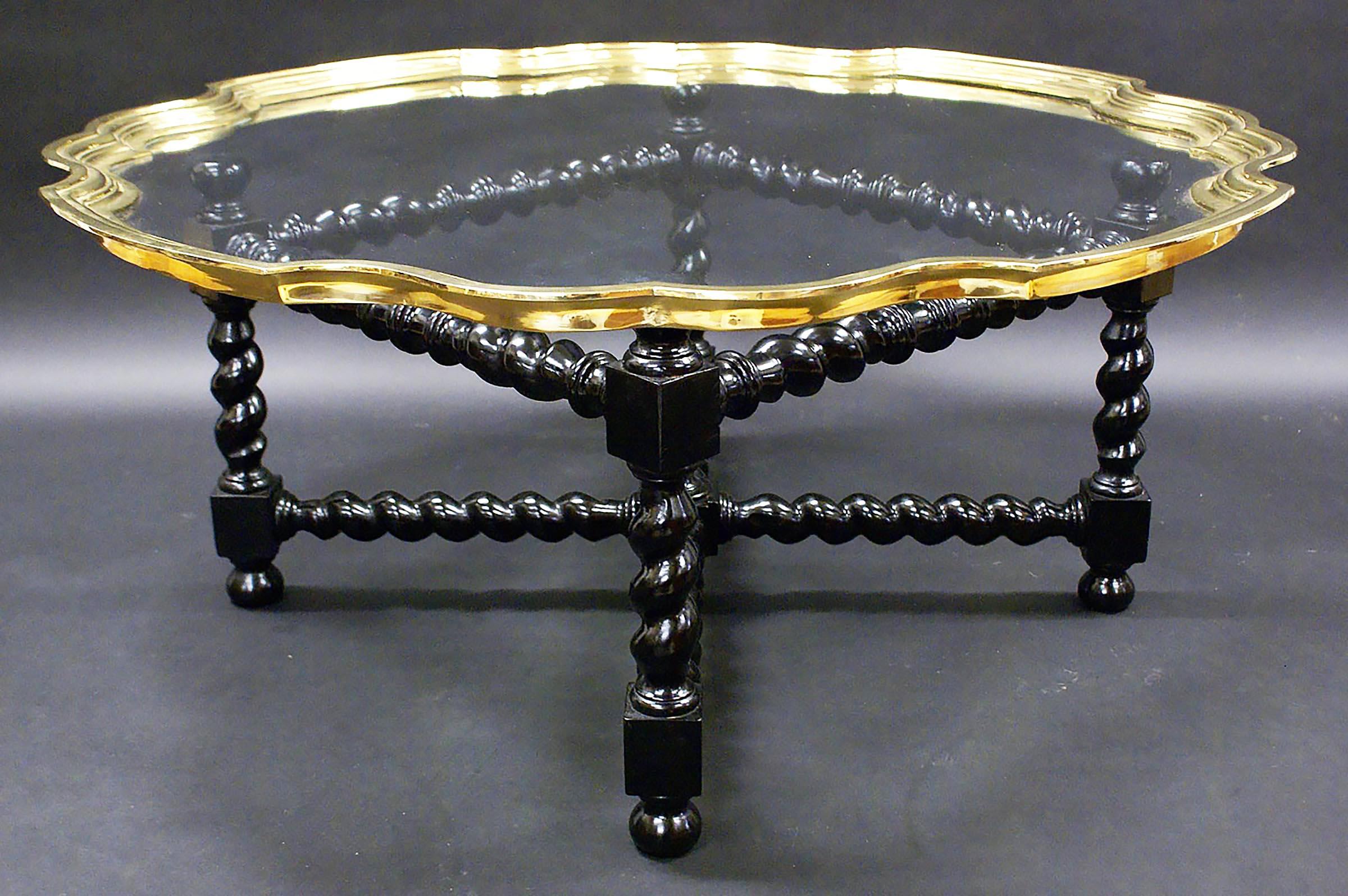 This striking and well-proportioned glass topped early 20th century. coffee table features a lovely brass pie crust shaped edge with a barley twist ebonized base and ‘X’ frame stretcher base, and was originally sold thru Harrods of London. The table