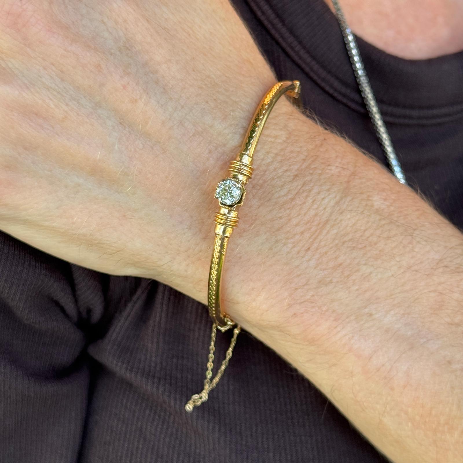 This handcrafted early 20th century 14 karat yellow gold bangle features a single old mine-cut diamond of approximately 0.68 carats as its focal point. The bangle showcases a braided design along the sides, highlighting intricate artisan