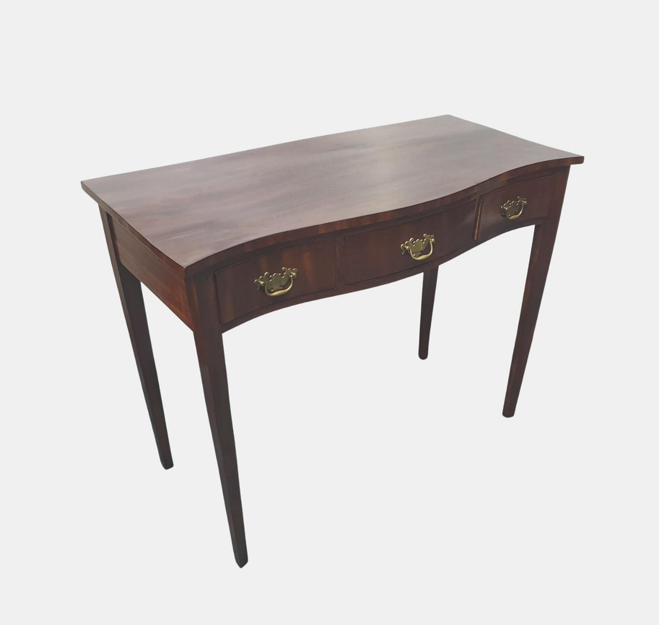 Early 20th century Edwardian mahogany side or hall table in the Georgian style, the moulded serpentine shaped front with moulded top above frieze with three drawers with decorative brass ring pulls supported on tapering square leg. 

Fully