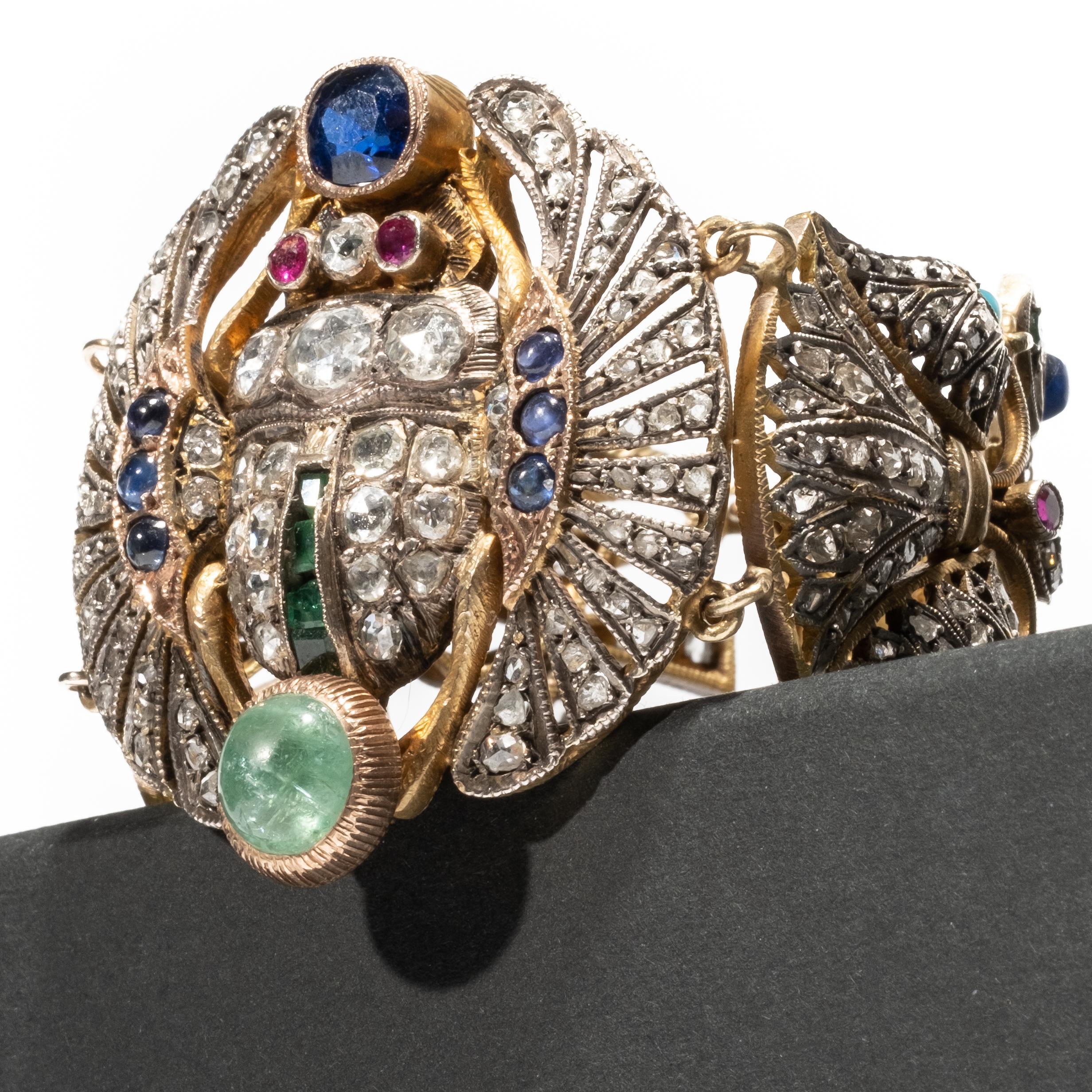 Early 20th Century Egyptian revival Silver and gold Diamond and gem-set scarab bracelet. Centered on a scarab, set with rose-cut diamonds, rubies, emeralds, and sapphires, joining ankh and lotus links set with diamonds, sapphires, turquoise, and