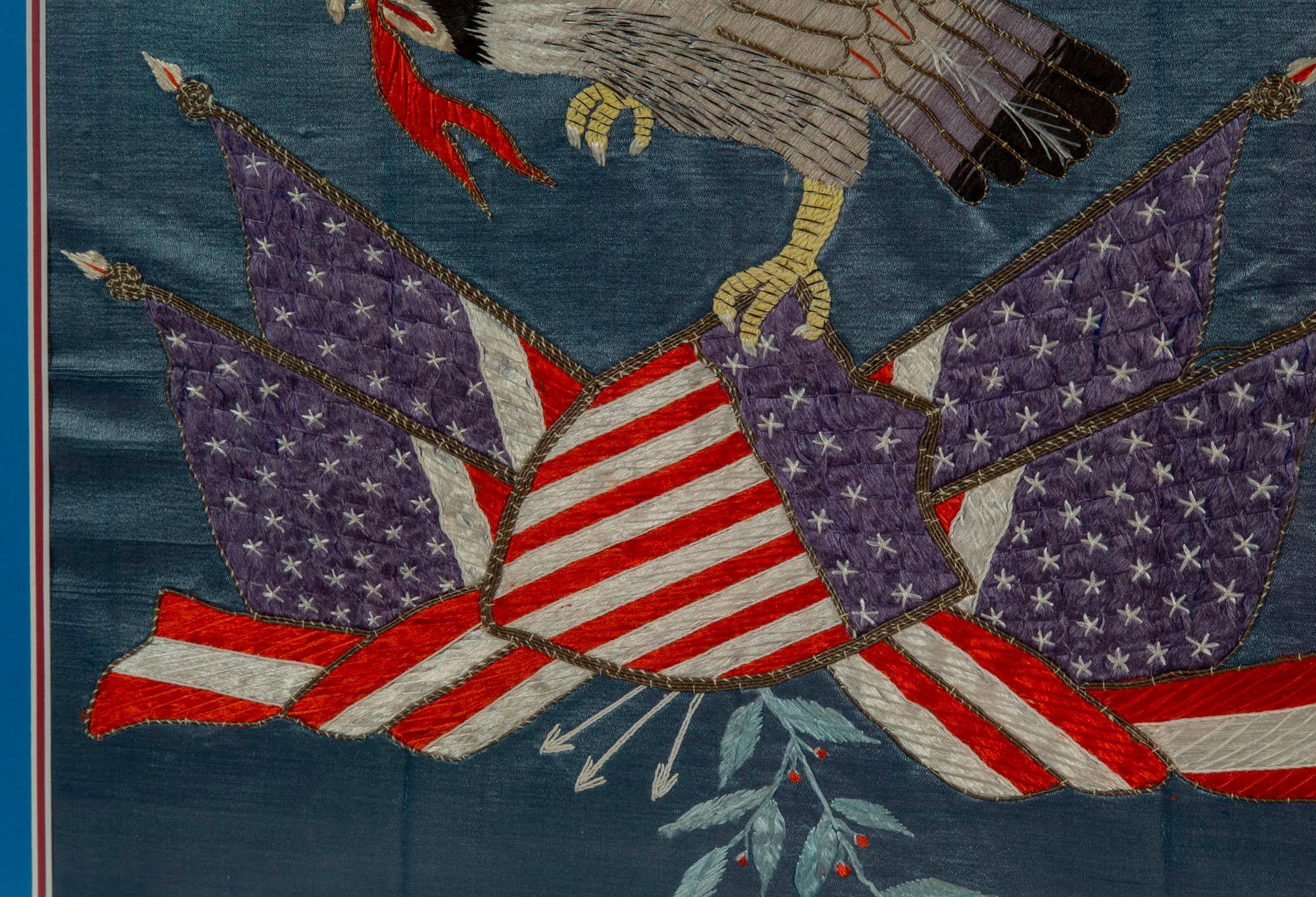 An early 20th century needlework picture of an eagle, holding a banner with the motto: 