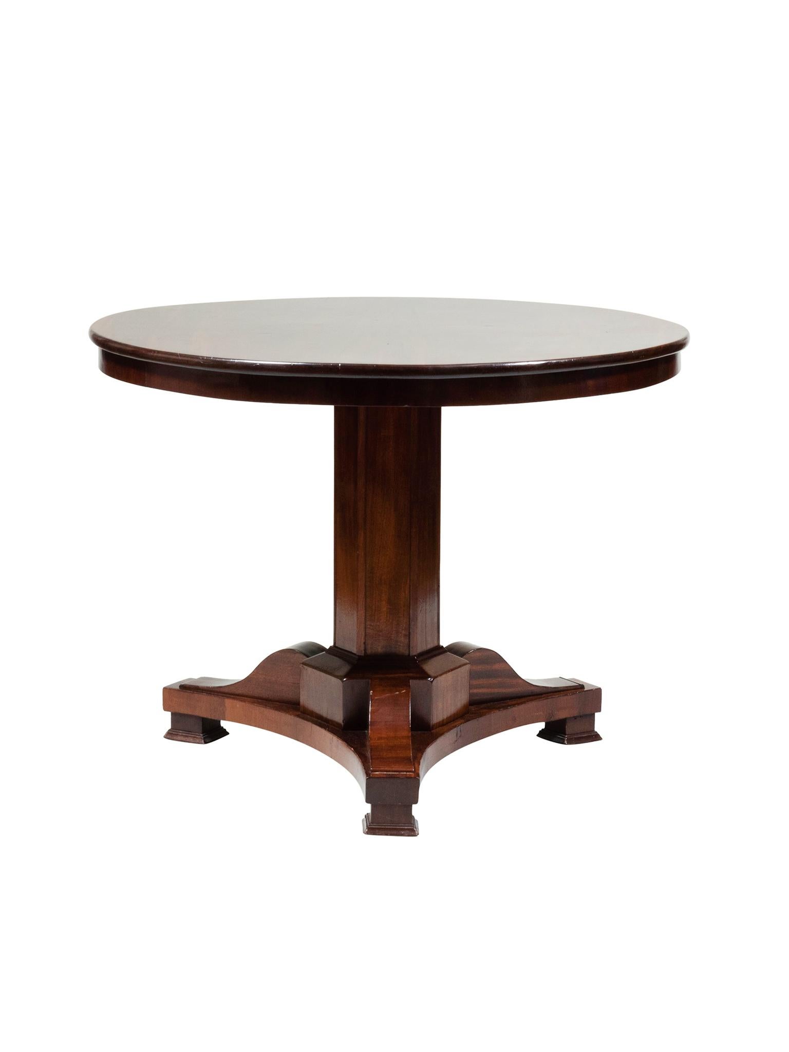 This round center table was made in the Early 20th Century in the Empire style. Its design is one of symmetry and balance: a classic circle atop a pedestal base. The mahogany wood has a warm red-brown tone and has been recently
