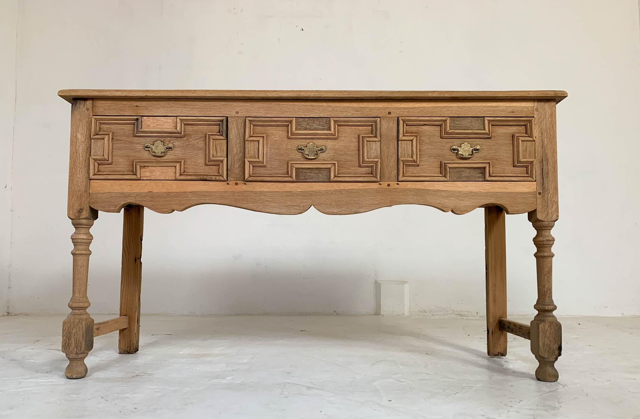 Three drawer bleached oak dresser base dating from early 20th century. It has original brass handles, turned front legs and straight back legs. The back two feet have some damage however this does not affect how the dresser stands. There is also a