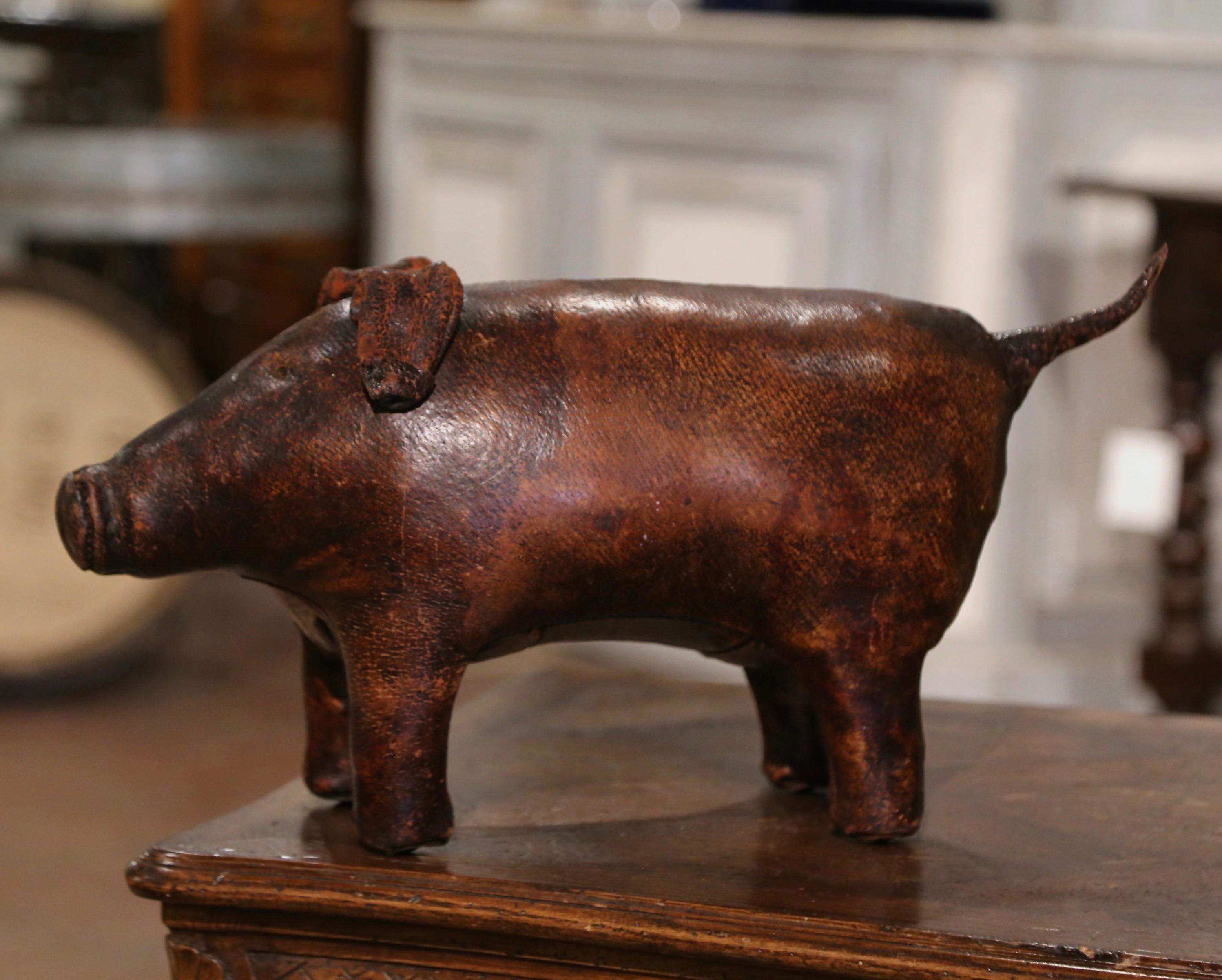 
Rest your feet on this cheerful and unique antique footstool. Crafted in England circa 1920, and shaped as a pig, the freestanding hog stands on his four legs and is recovered with the original patinated brown leather; the stool is complete with