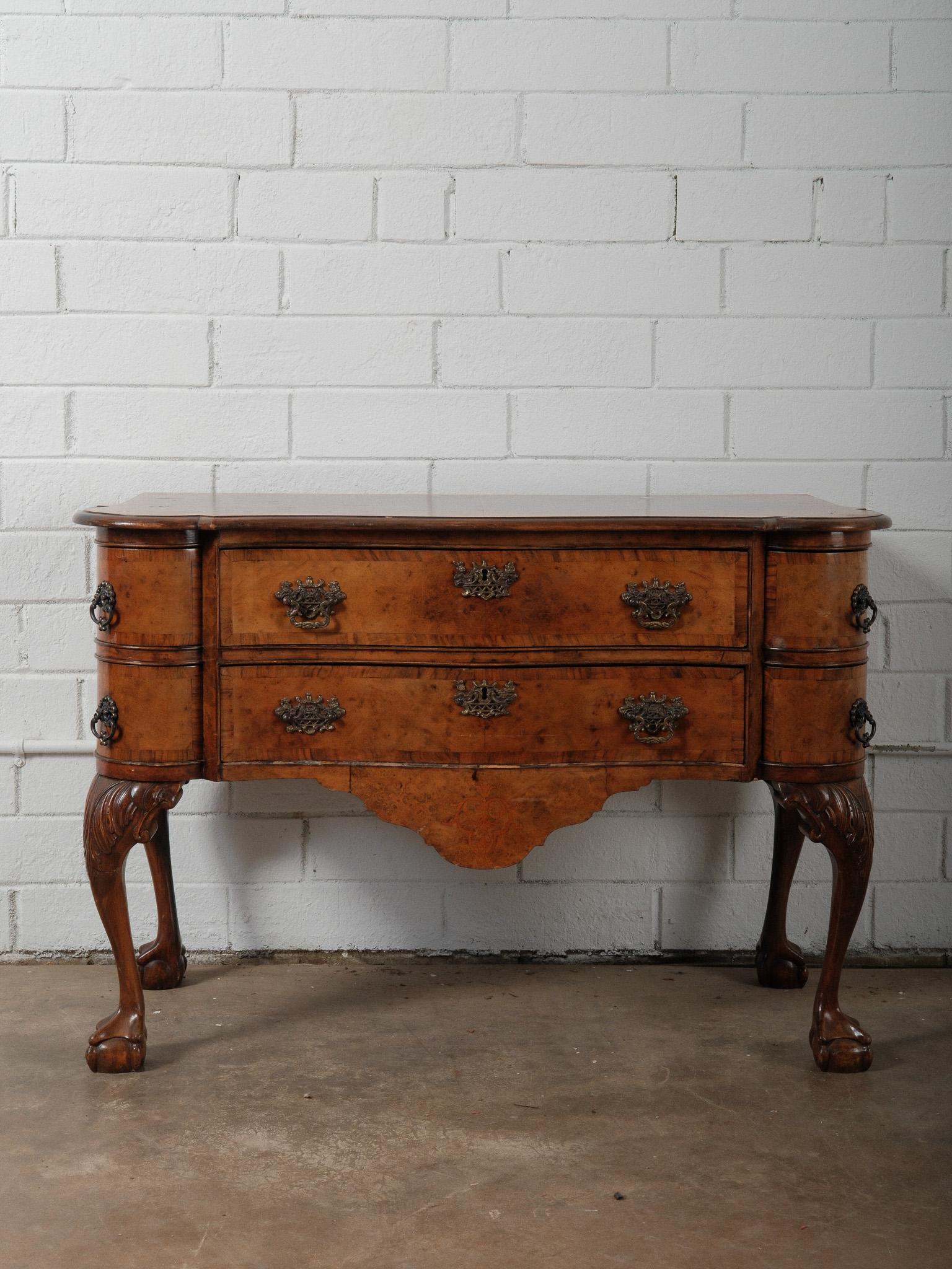 A finely crafted early 20th-century English Chippendale-style lowboy or small sideboard, constructed in burl walnut and richly detailed throughout. The serpentine front and bow-shaped sides flow elegantly into four carved cabriole legs terminating