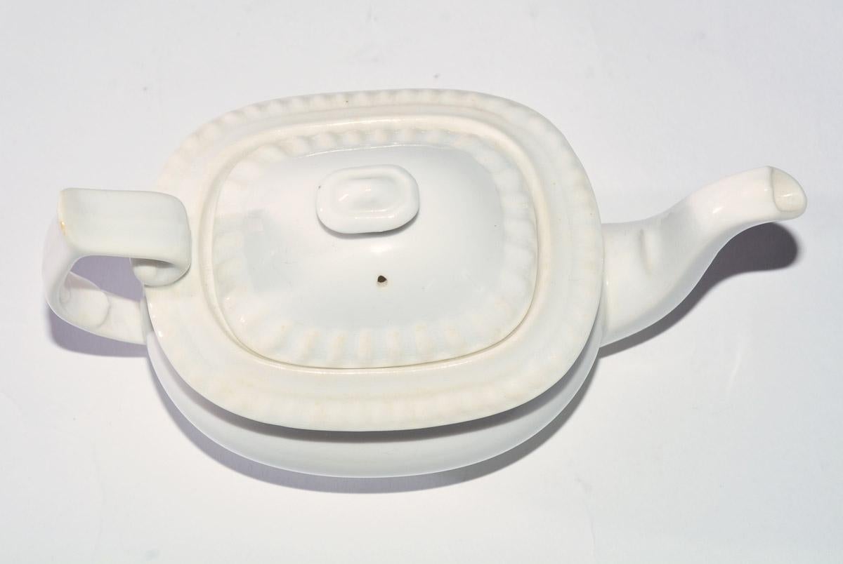 The early 20th Century English petite child's teapot is decorated around the opening with fluting as is the rim of the lid. Both pieces of the white teapot are marked 