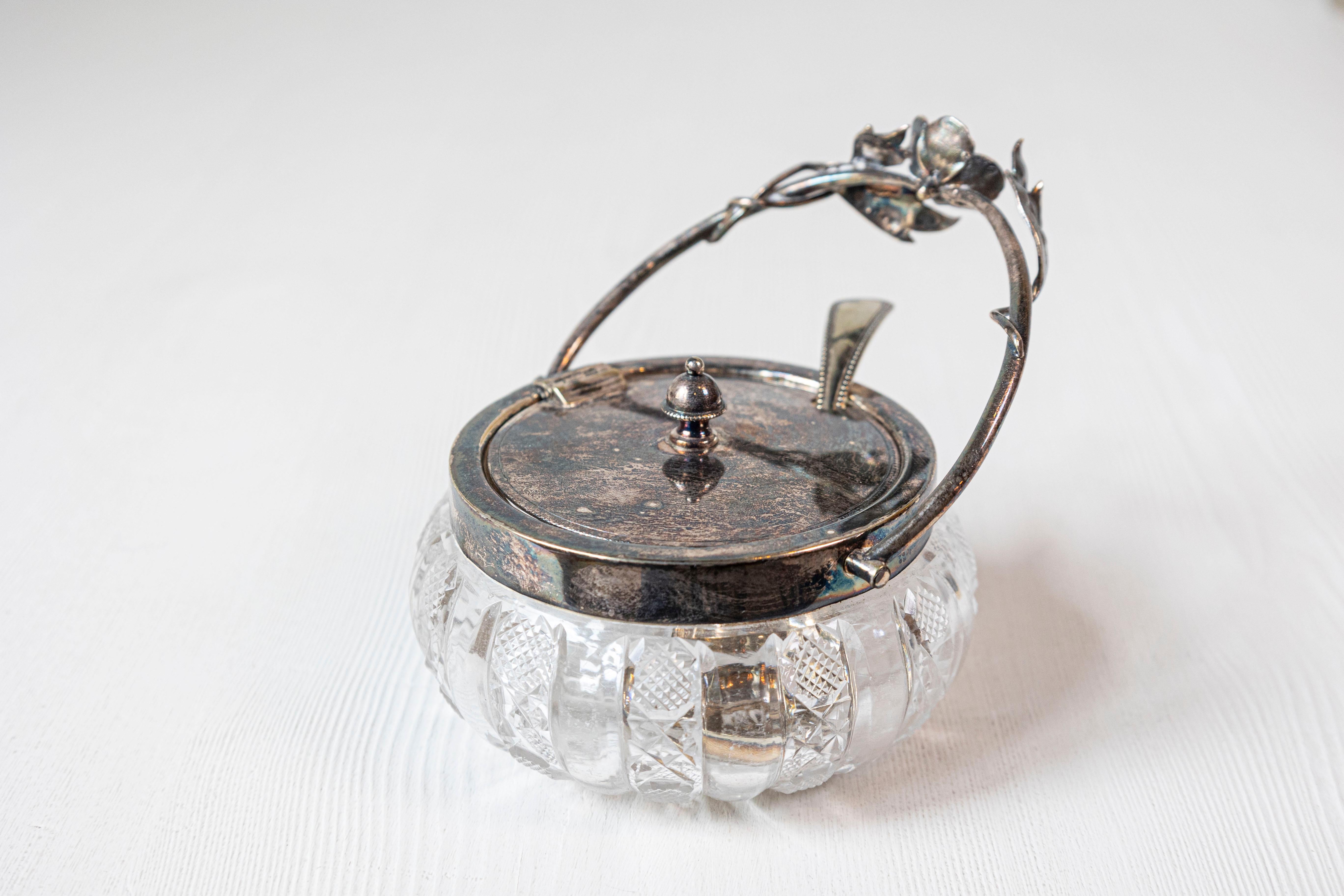 A charming early 20th century English sugar bowl featuring a beautifully cut glass body and silver-plated lid with a matching floral-accented handle. Petite in scale yet rich in detail, this piece was likely part of a formal tea service, used to