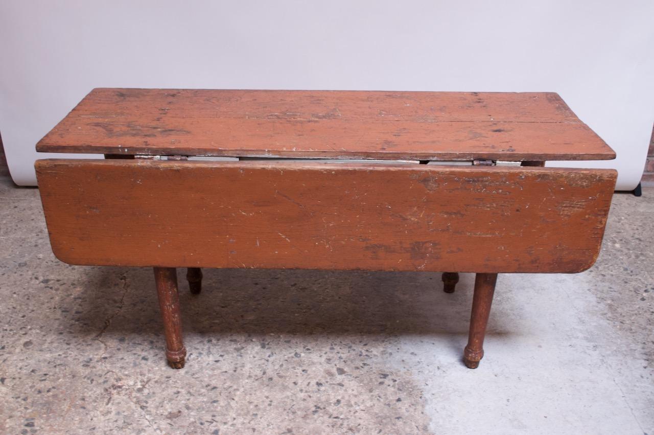 Table de ferme rustique (vers 1910-1920, Angleterre) composée d'un plateau en planches peintes et de pieds tournés (la peinture teintée terre cuite est d'origine). Deux vantaux supplémentaires peuvent être étendus en libérant deux supports en bois.