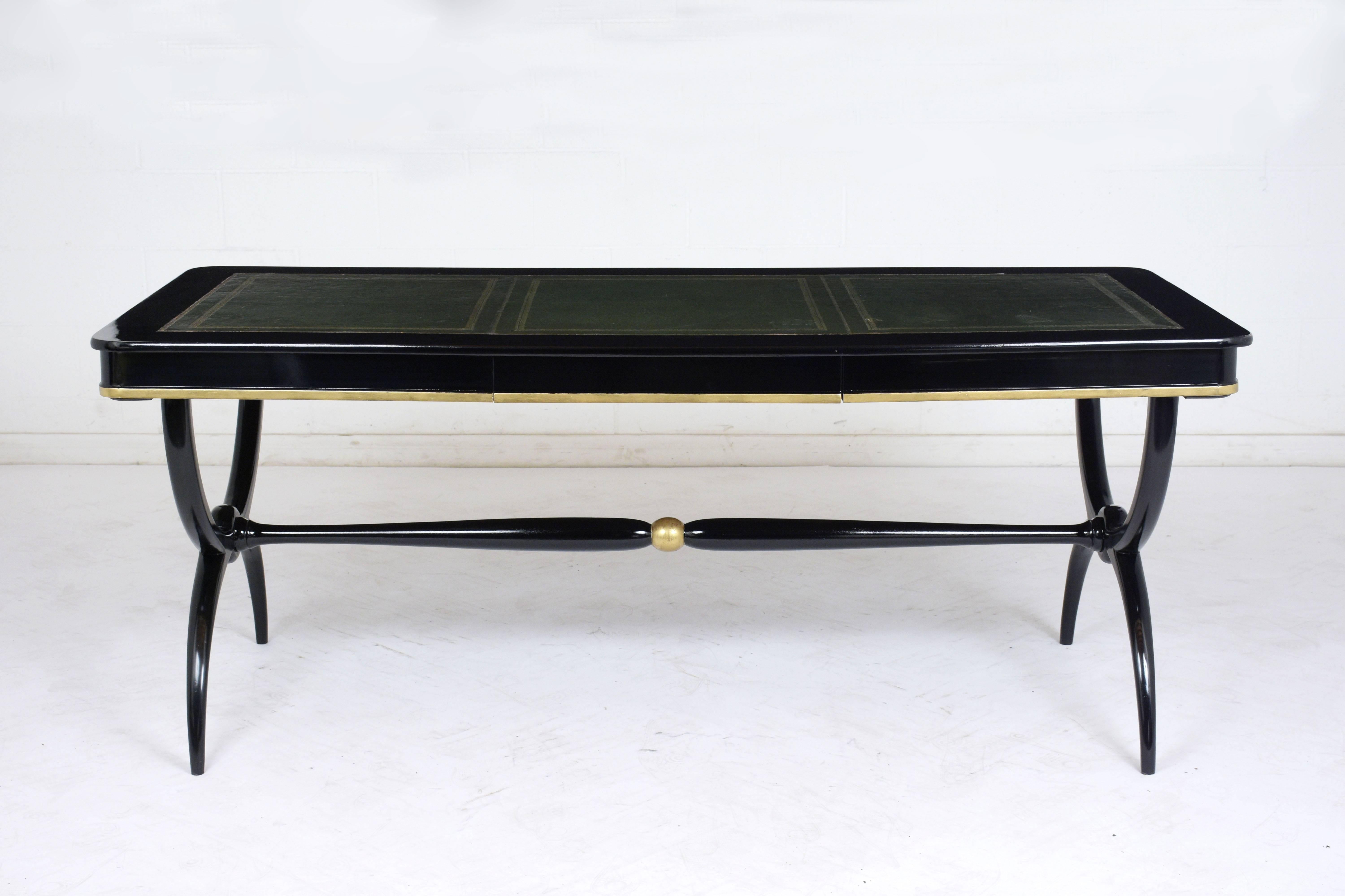 This 1900s English Regency-style desk is made of mahogany wood with an ebonized and lacquered finish. The top of the desk features the original embossed leather insert with gilt trim details. There is a single drawer in the center with a gilt accent