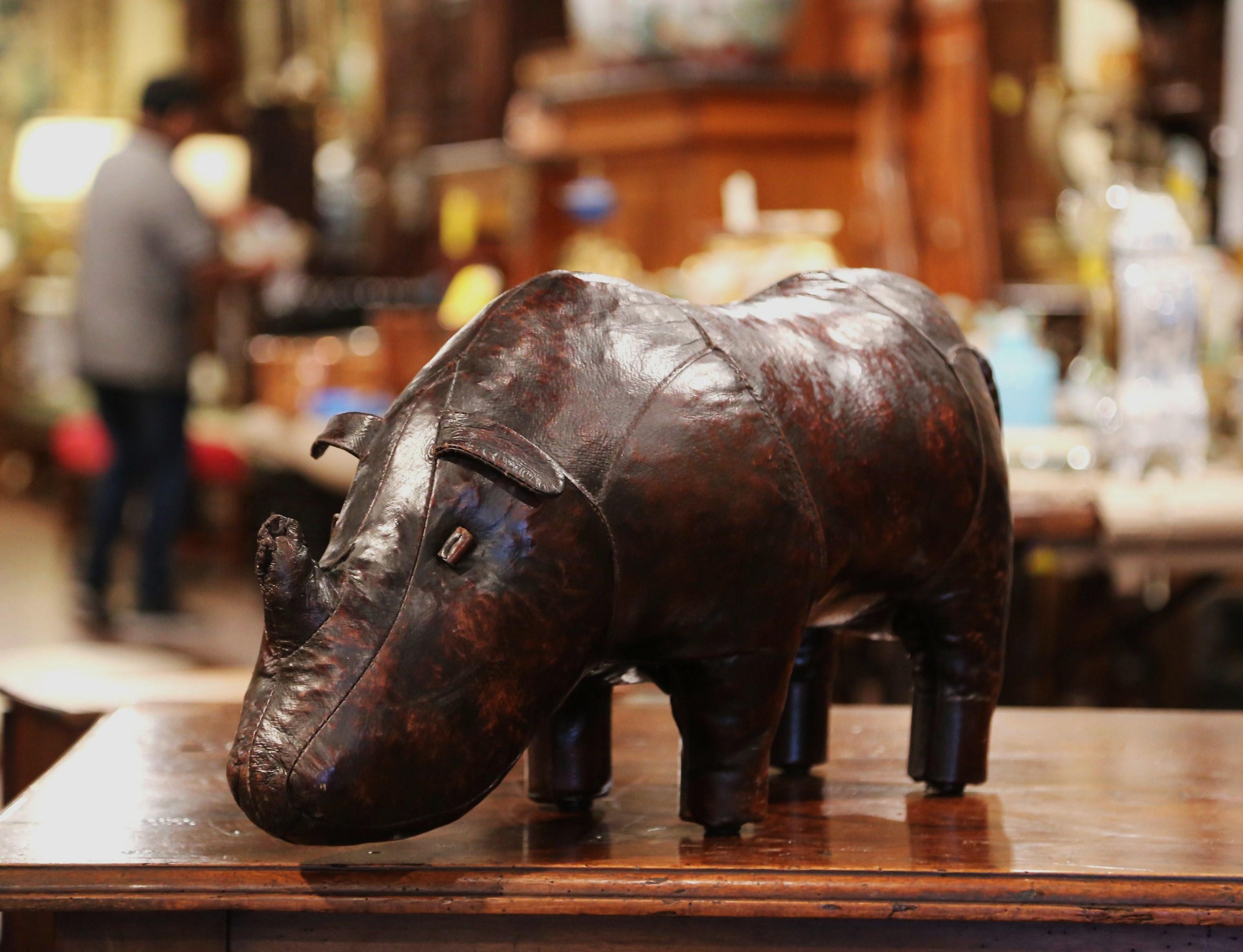 This beautiful, antique footrest was crafted in England, circa 1920. Shaped as a rhinoceros, the unique, freestanding, sculptural stool has been recovered with its original patinated brown leather. The Big Five sculpture is in excellent condition