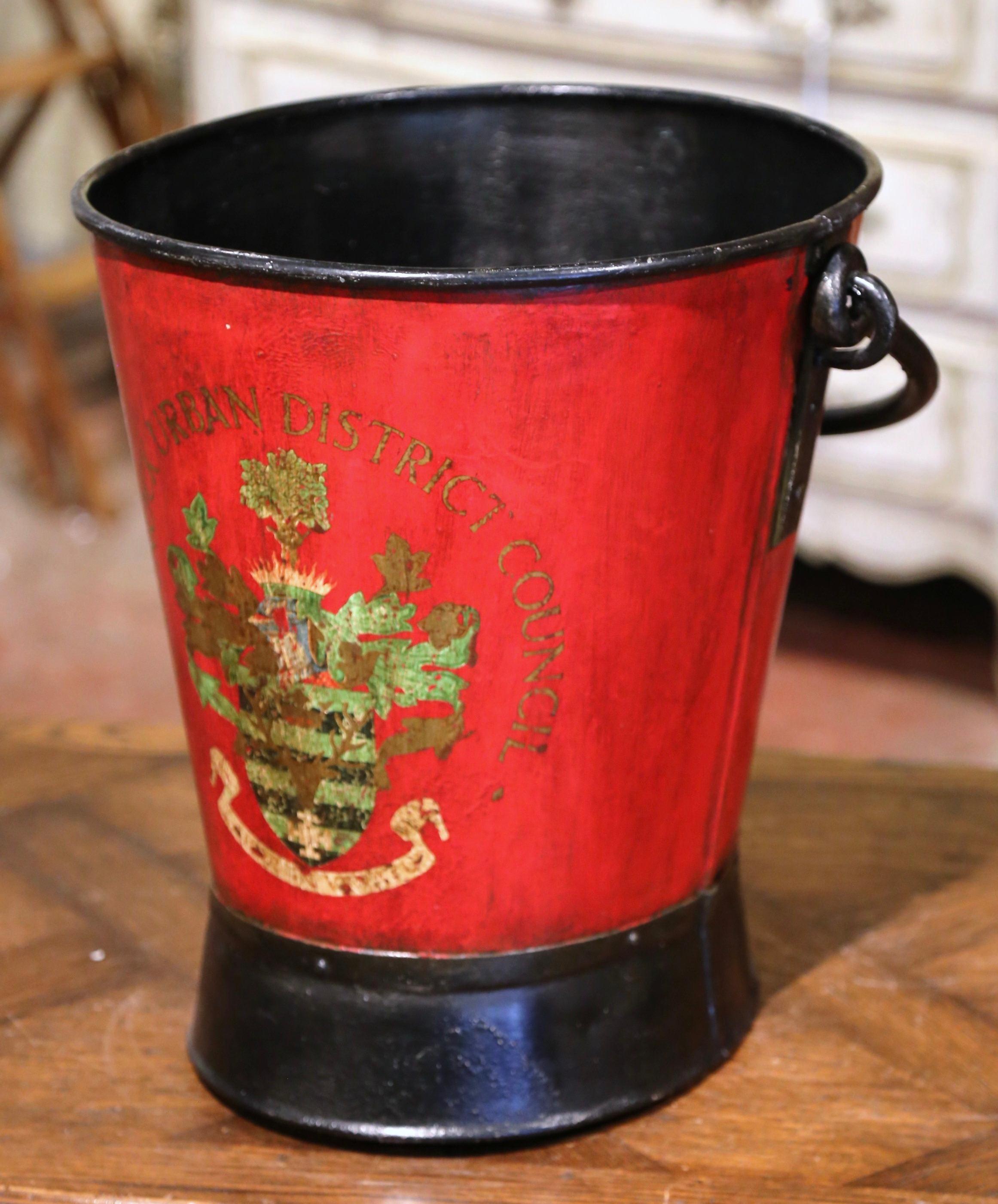 Place this large, colorful antique stand at your front door or in your mudroom to collect umbrellas, canes or other accessories; created in England circa 1920, the metal bucket with top and side handles, is decorated with a hand painted crest