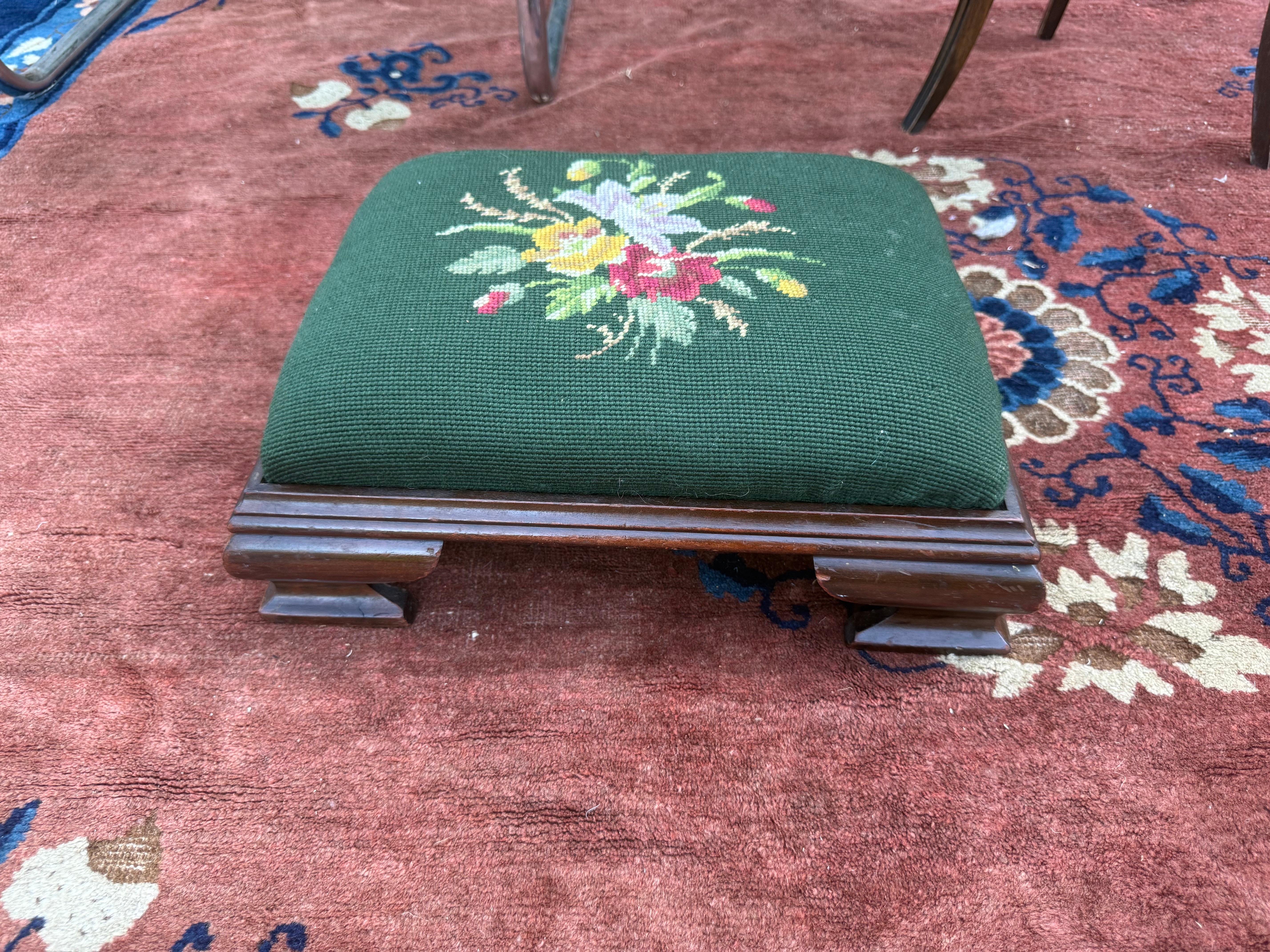 Dieser exquisite englische Hocker mit Nadelspitze ist ein Beispiel für die raffinierte Handwerkskunst des britischen Kunstgewerbes des frühen 20. Jahrhunderts. Das Stück zeigt ein wunderschön handgesticktes Blumenbouquet in leuchtenden Farben -