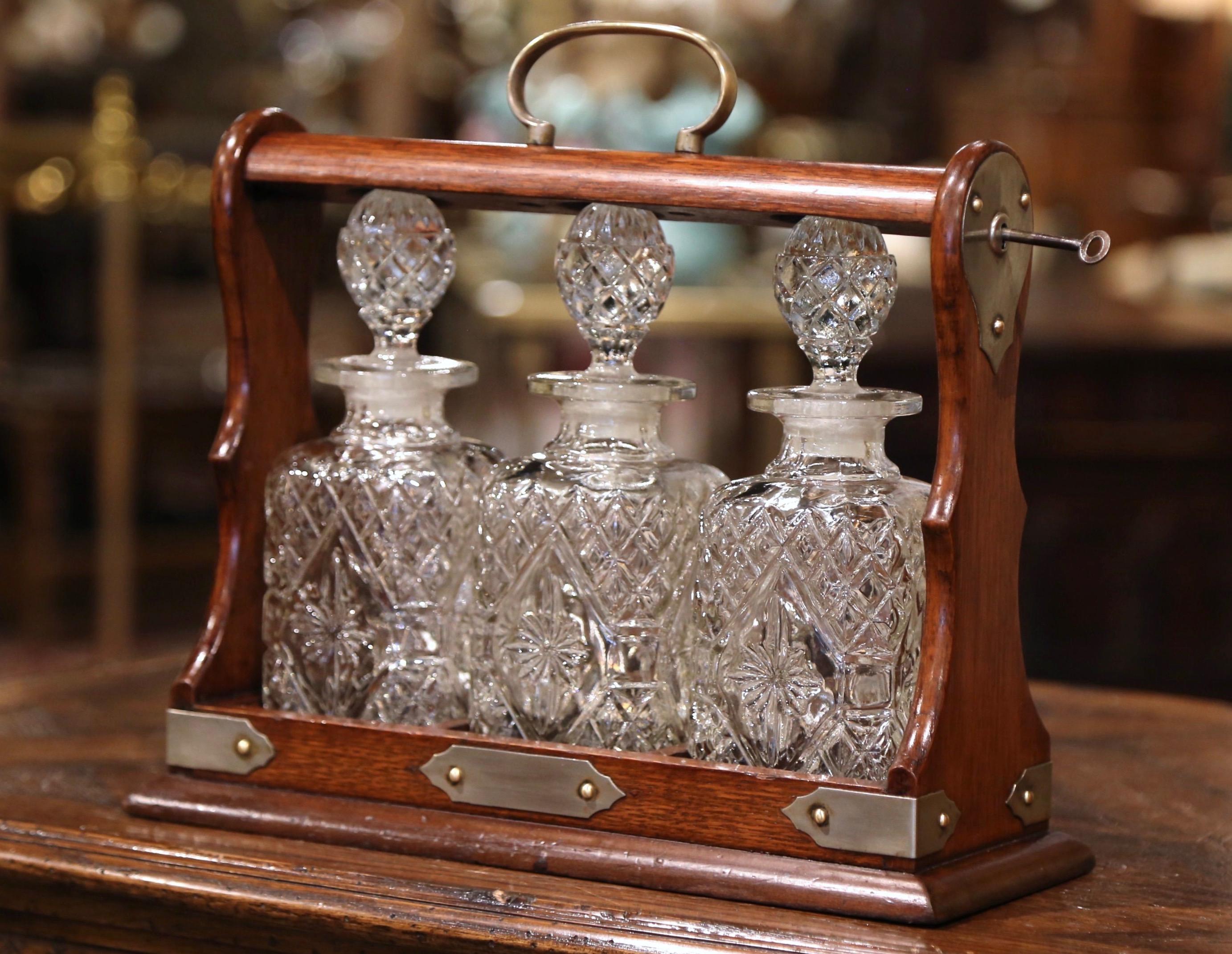 Entertain in style with this antique oak Tantalus and crystal decanter set; crafted in England, circa 1920, the liquor set is unique with nickel silver side mounts and its original ball faceted swivel locking mechanism with key, and embellished with