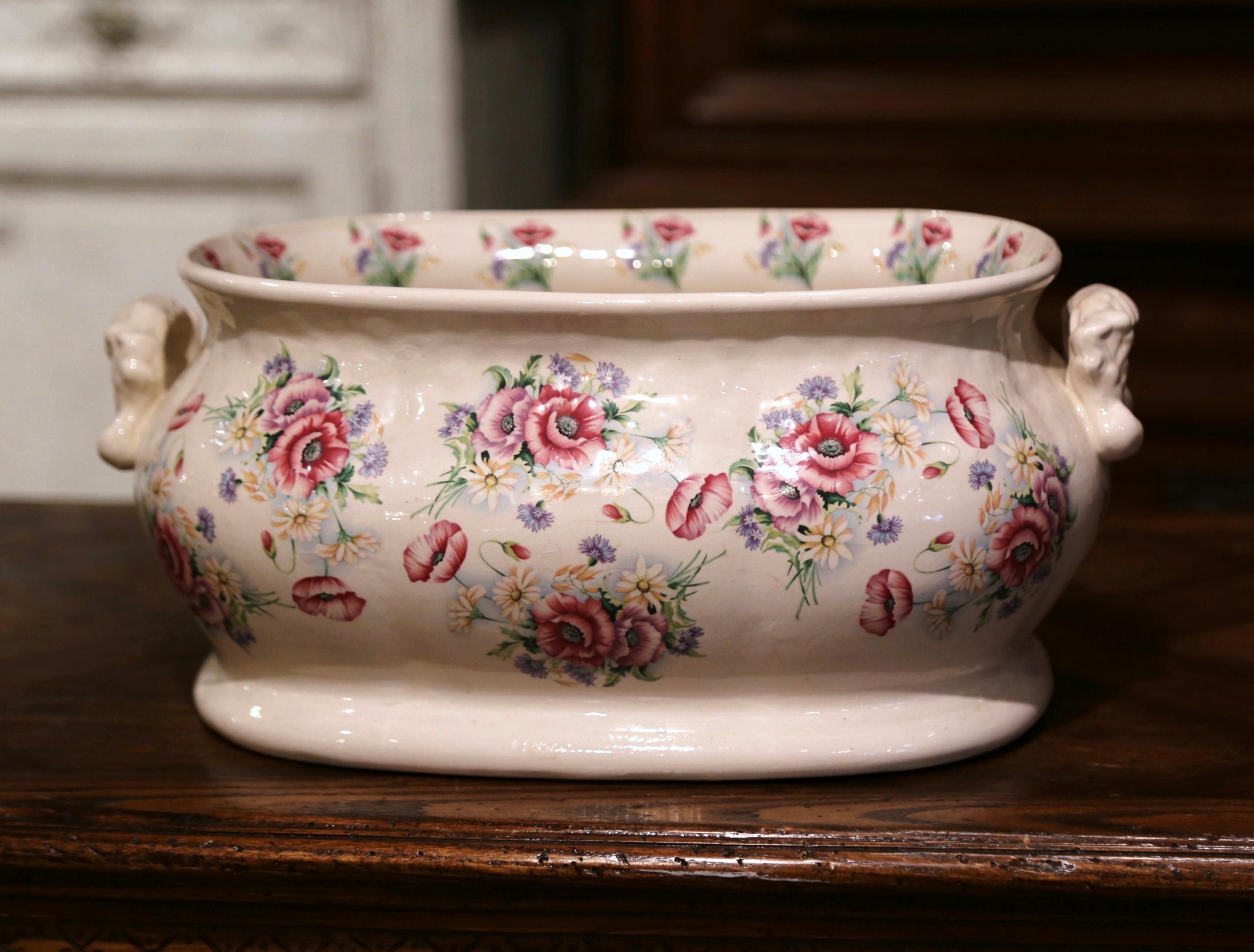 Crafted in England circa 1920 and oval in shape with bowed sides, the antique porcelain basin features two side handles and is hand painted with floral motifs in the pink and pale blue palette. This elegant and colorful jardinière is in excellent