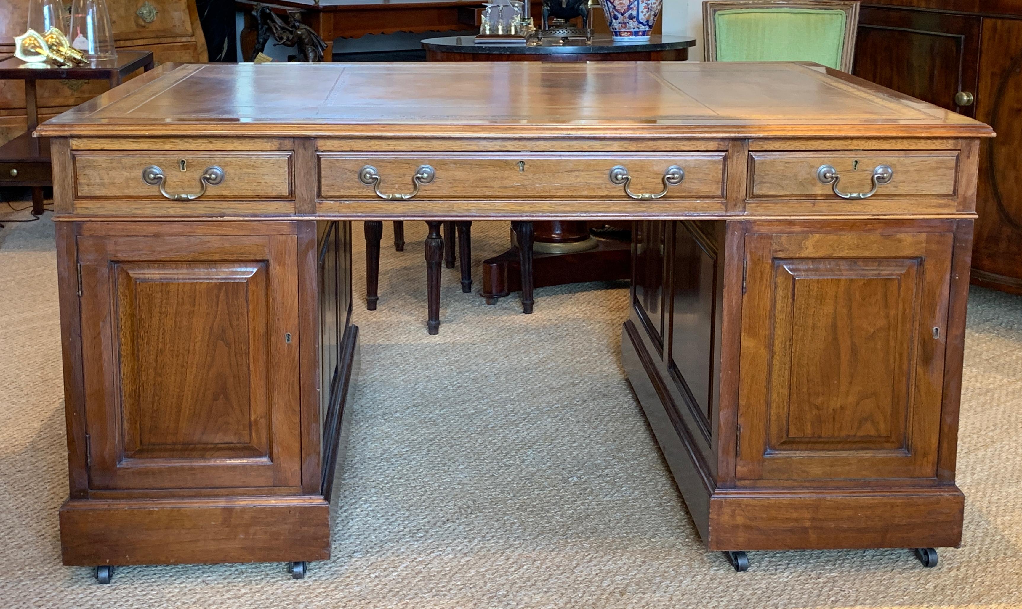 A magnificent early 20th century English mahogany and tooled leather topped partner’s desk by Hobbs and Co. with opposite facing cabinet and drawer pedestal bases on casters and two small and single larger drawers on both sides of the top.