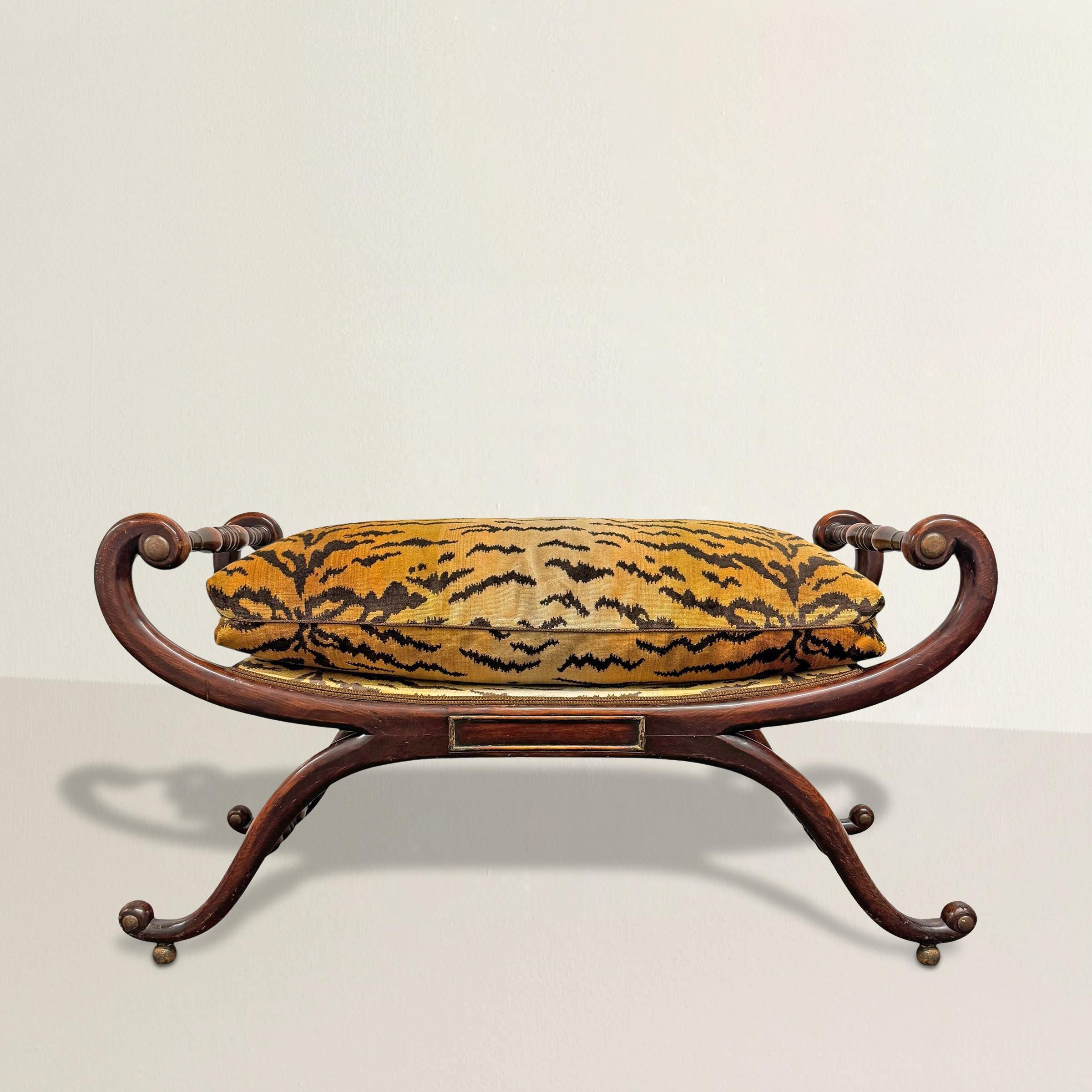 An early 20th-century stool that channels the sweep of English Regency design but feels as current as a Fifth Avenue apartment done to the nines. The curule frame, carved from maple, arcs in sculptural curves, its scrolled ends and ball feet traced