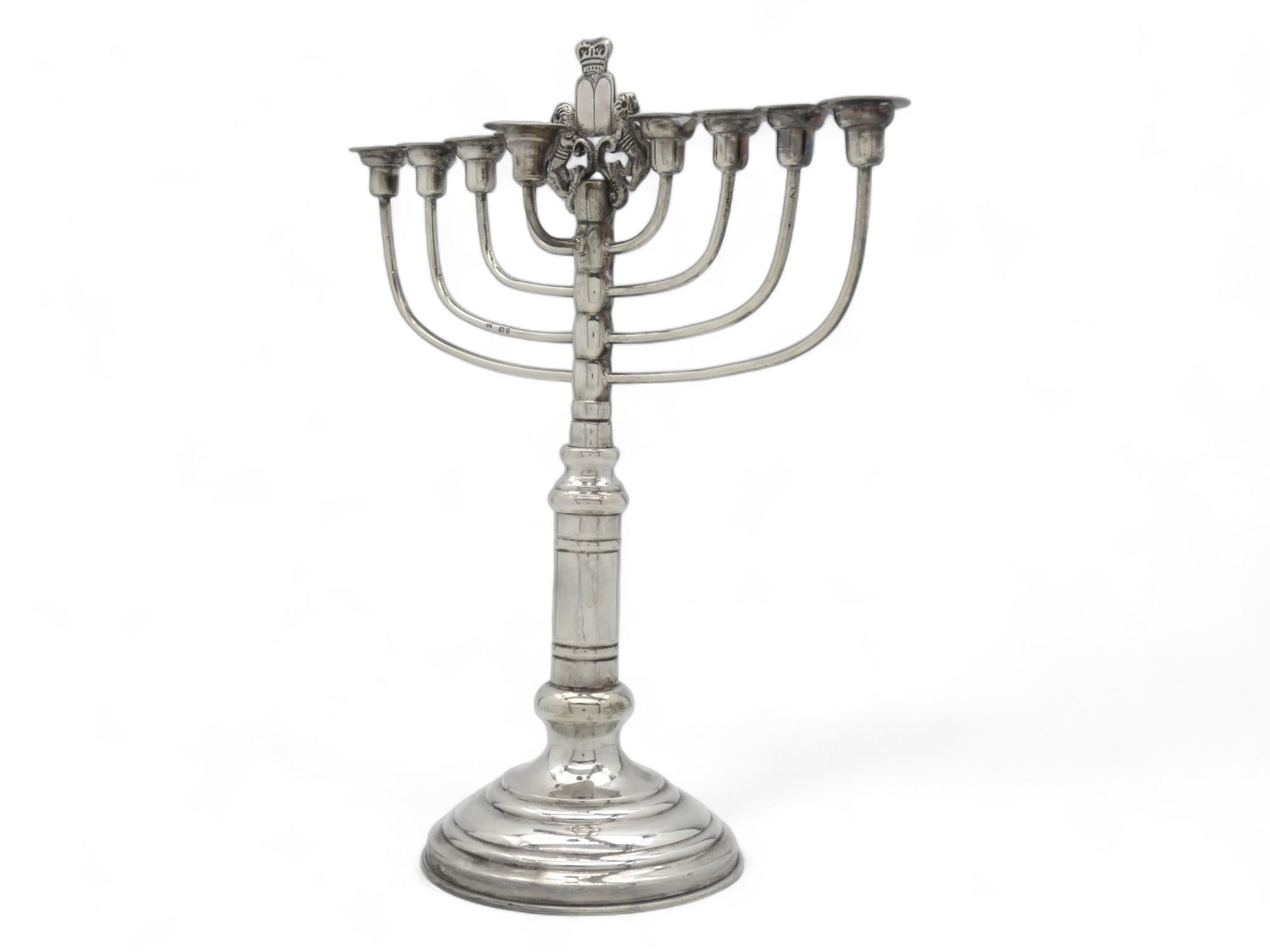 Standing Hanukkah lamp made in London, England, 1926. Stamped and marked with English silver hallmarks for 1926, London. In the center stands the “Lion of Judah,” a pair of recumbent lions raised on pedestals, carrying the Ten Commandments, topped