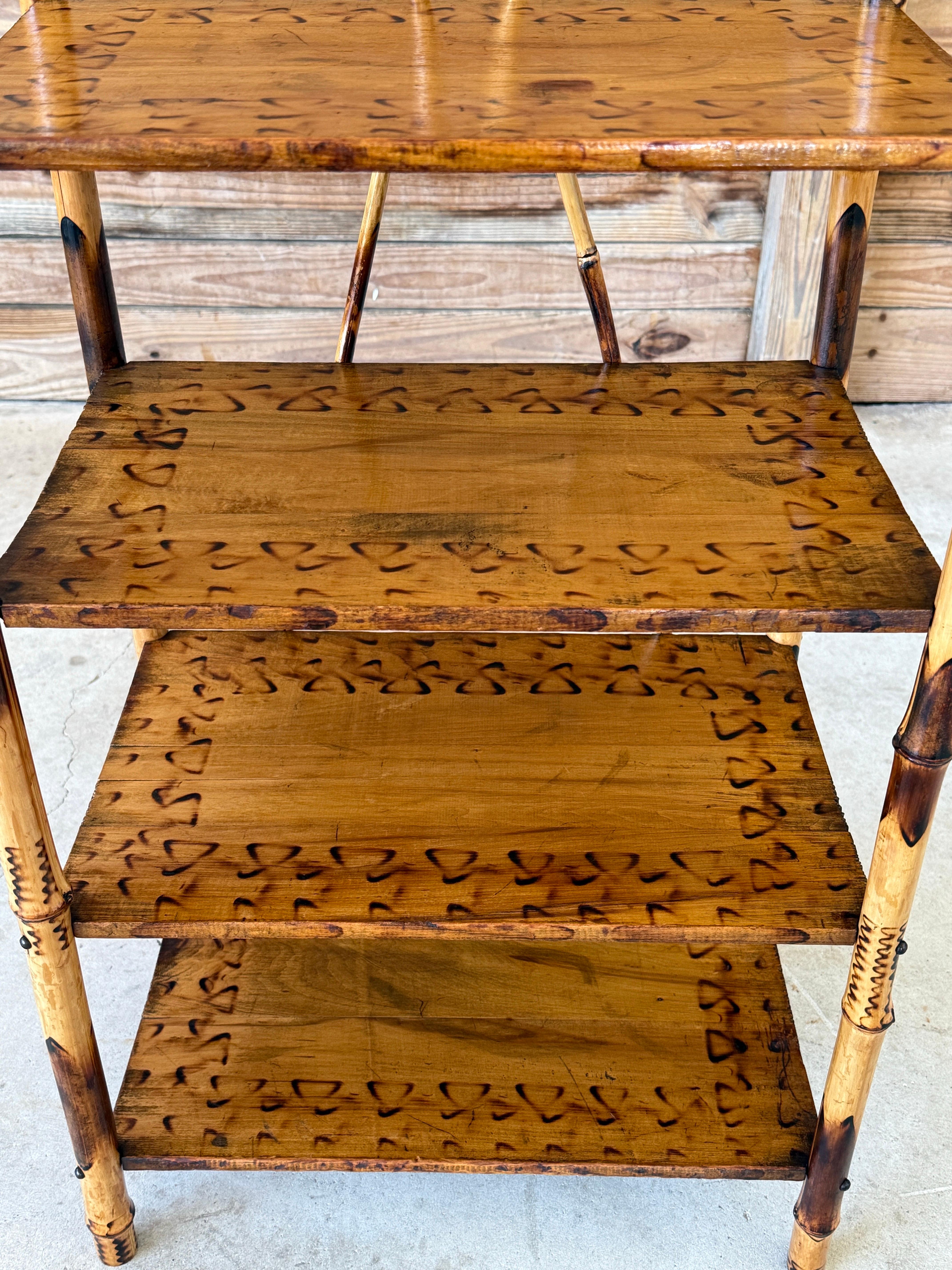 A charming early 20th century English bamboo etagere, beautifully restored and featuring four wood shelves with decorative burnt-in motif edging and turned spindle gallery top.
The scorched bamboo frame adds character and warmth, while the overall