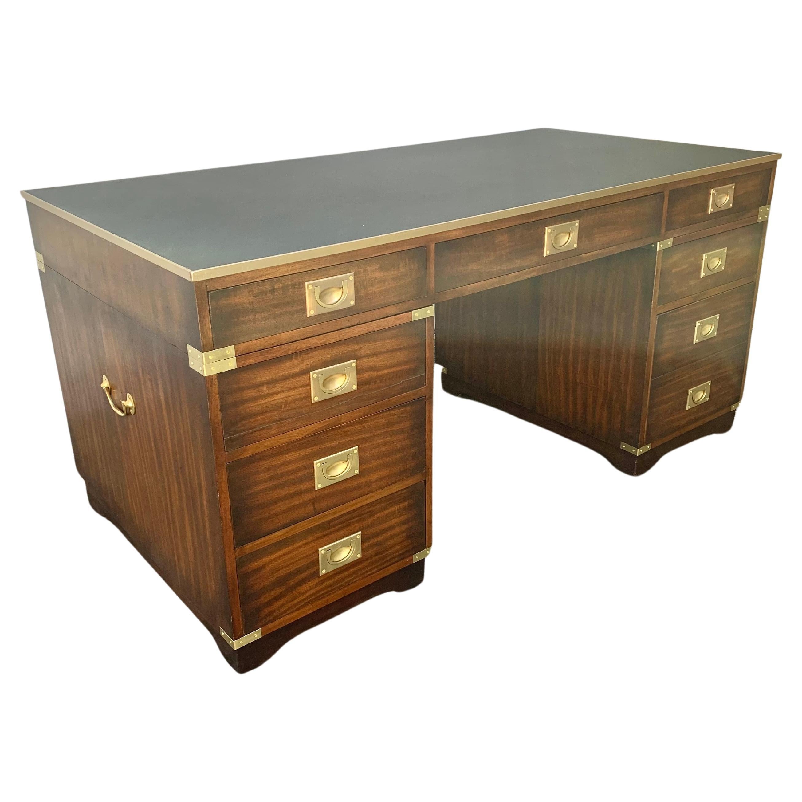 This Antique English Campaign Desk was crafted by artisans from walnut in the early 20th Century. The desk features a brass banded black leather top consisting of three drawers that rest on two sets of pedestal drawers, one being a double drawer.