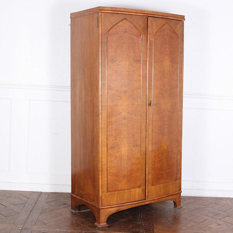 A smaller-scale English two-door bowfront wardrobe or armoire with book-matched figured walnut door fronts and Gothic details, the doors opening to a rod for hanging clothes and an upper shelf. A better-quality piece with solid walnut plank sides